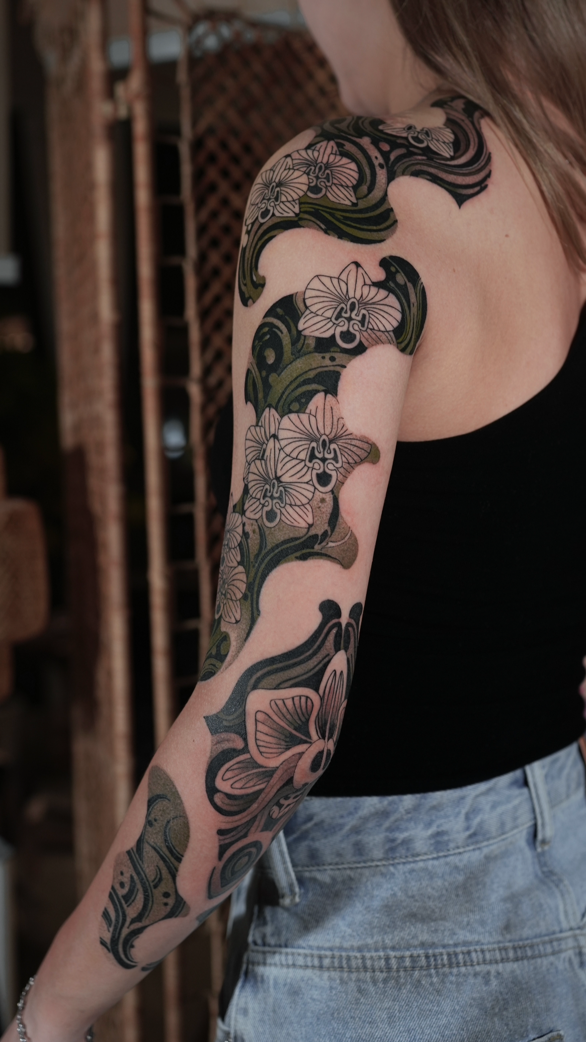 Close-up of a person's arm and shoulder with a large, detailed black and pink floral tattoo extending from the shoulder down the arm.