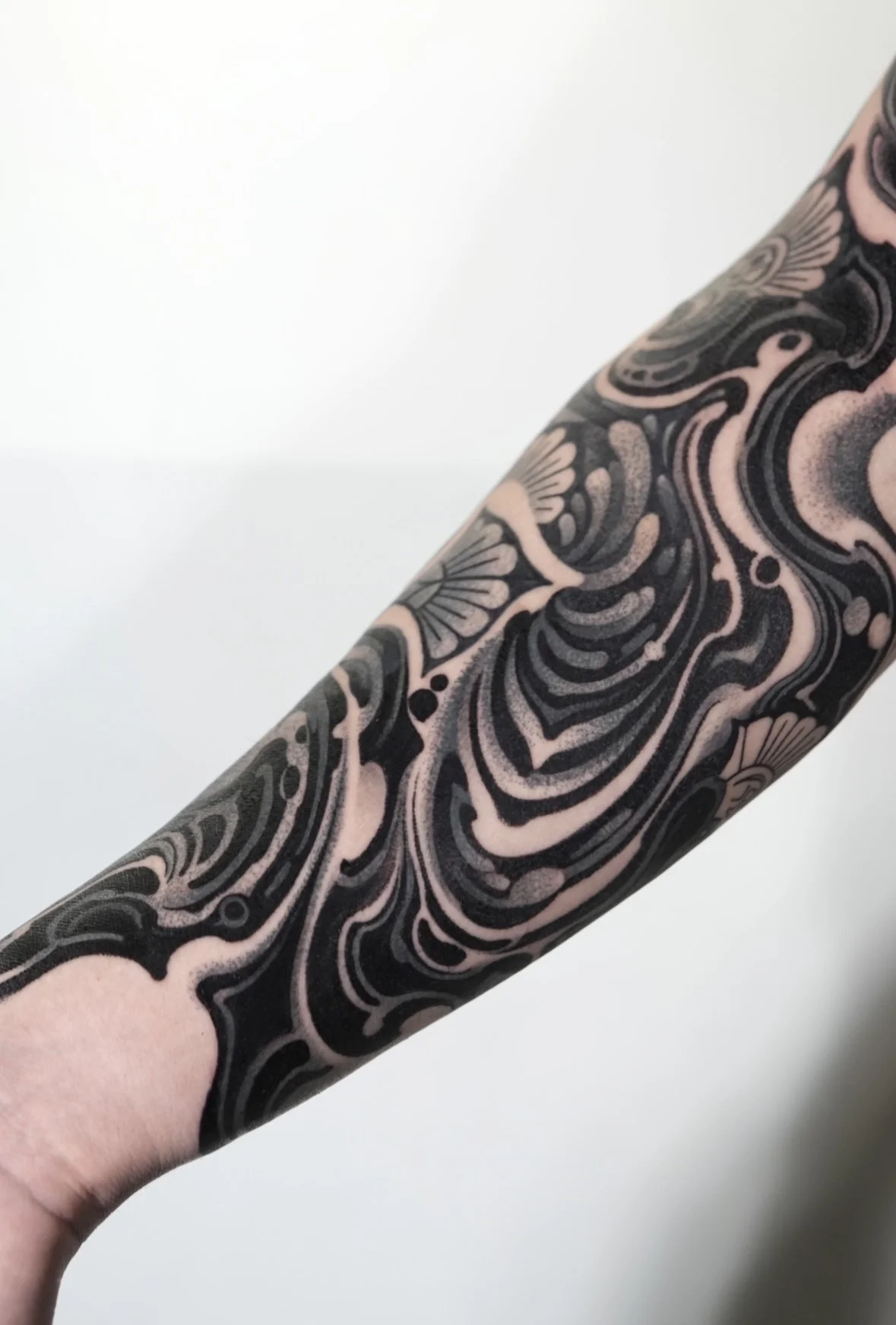 Close-up of a person's arm covered in intricate, black and tattooed swirly designs and patterns.