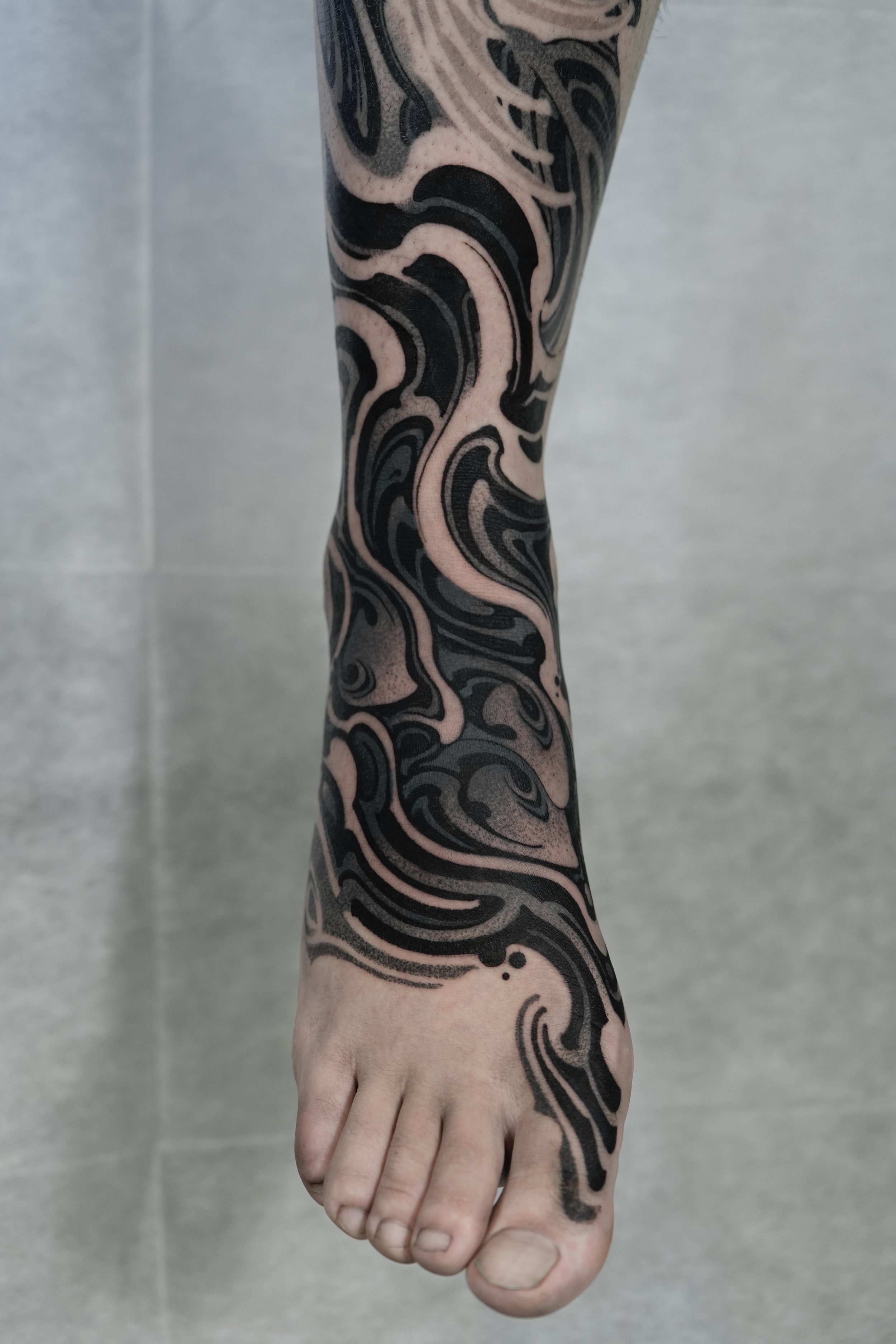 A person's arm and hand with a swirling black and gray tattoo extending from the shoulder to the fingers.