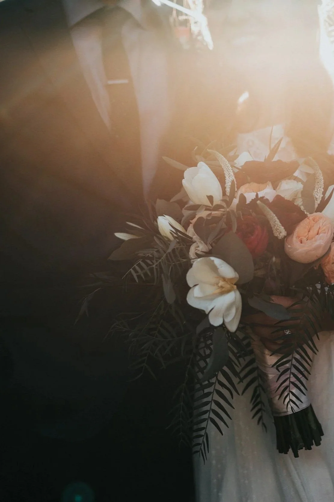 A bouquet of flowers with white tulips, roses, and greenery wrapped in white paper.