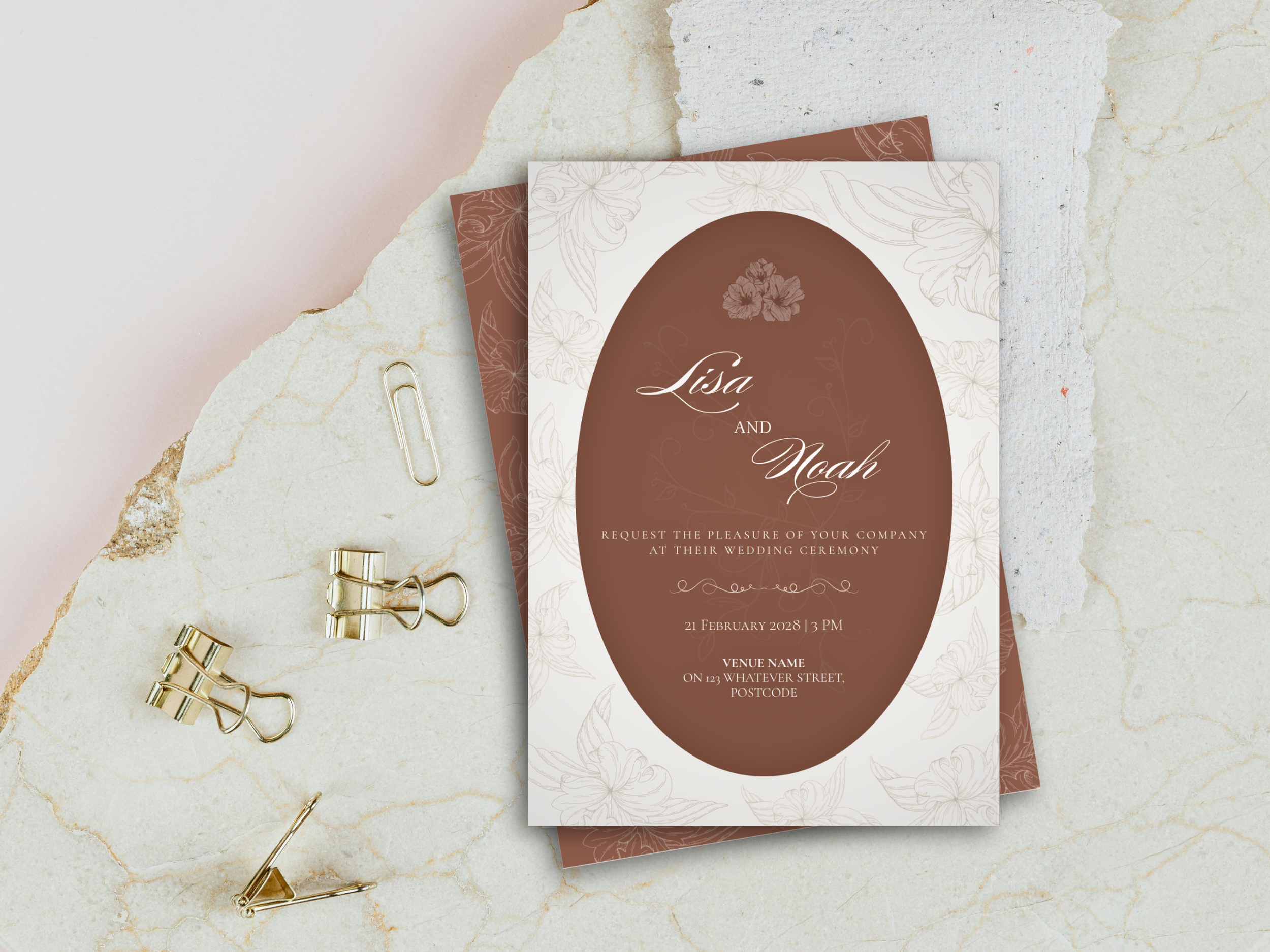 Wedding invitation card with floral design for Lisa and Noah, details of the wedding ceremony, and some gold clips and a paper clip on a marble surface.