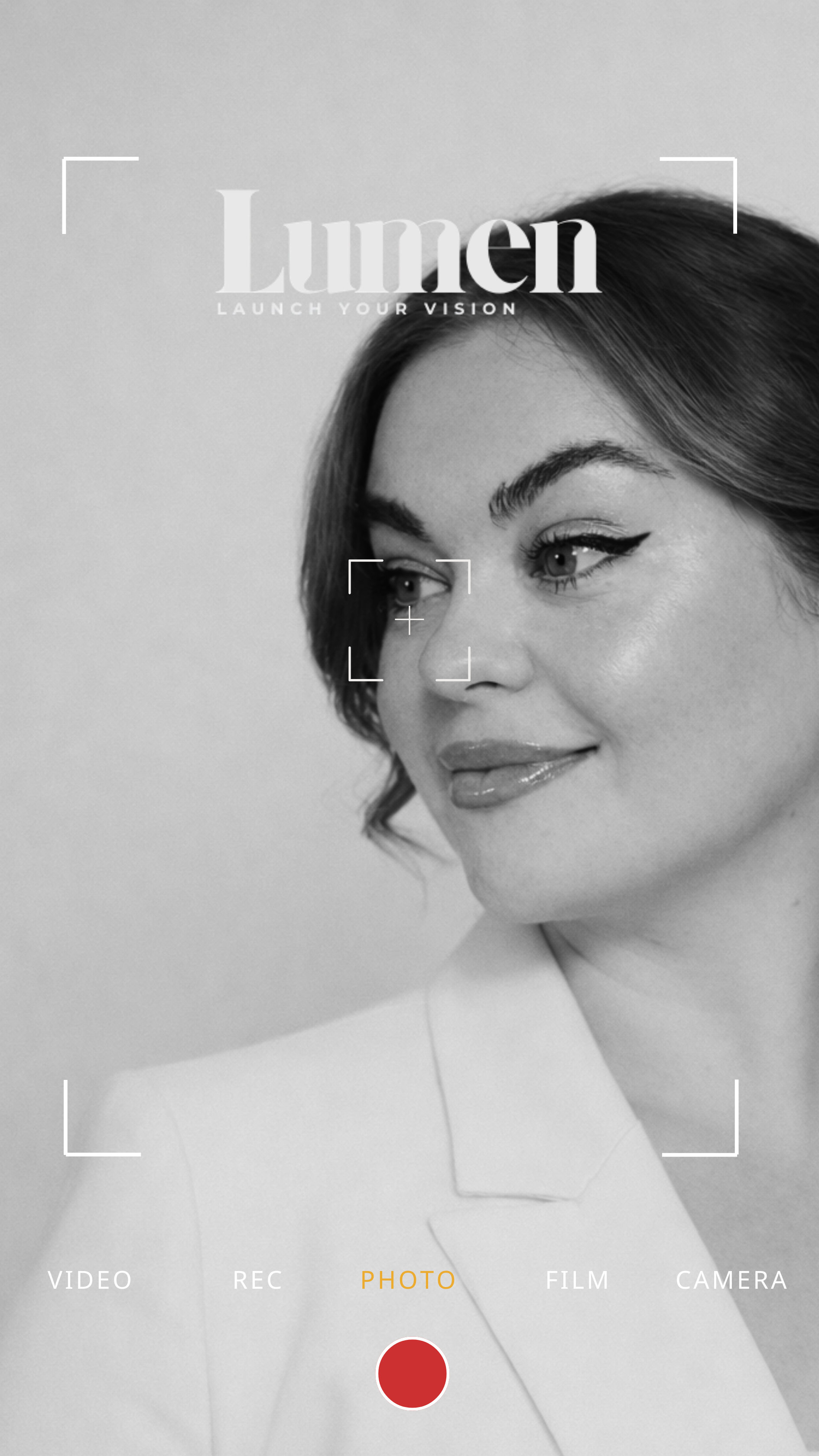 Black and white photo of a woman with makeup, smiling gently, with the words "Lumen Launch Your Vision" overlaid at the top, and camera interface options at the bottom.