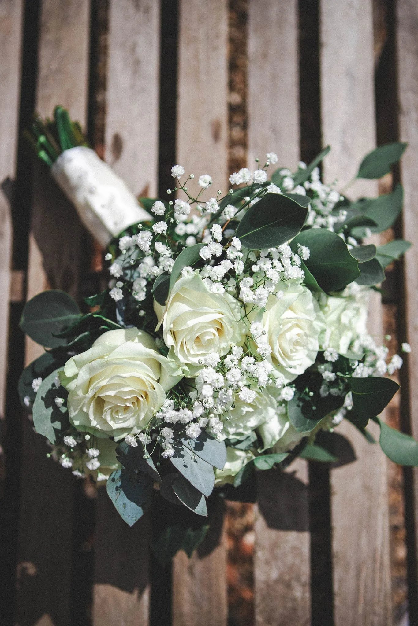 A wedding bouquet with white roses, Baby's Breath flowers, and green leaves, attached to a black metal fence.