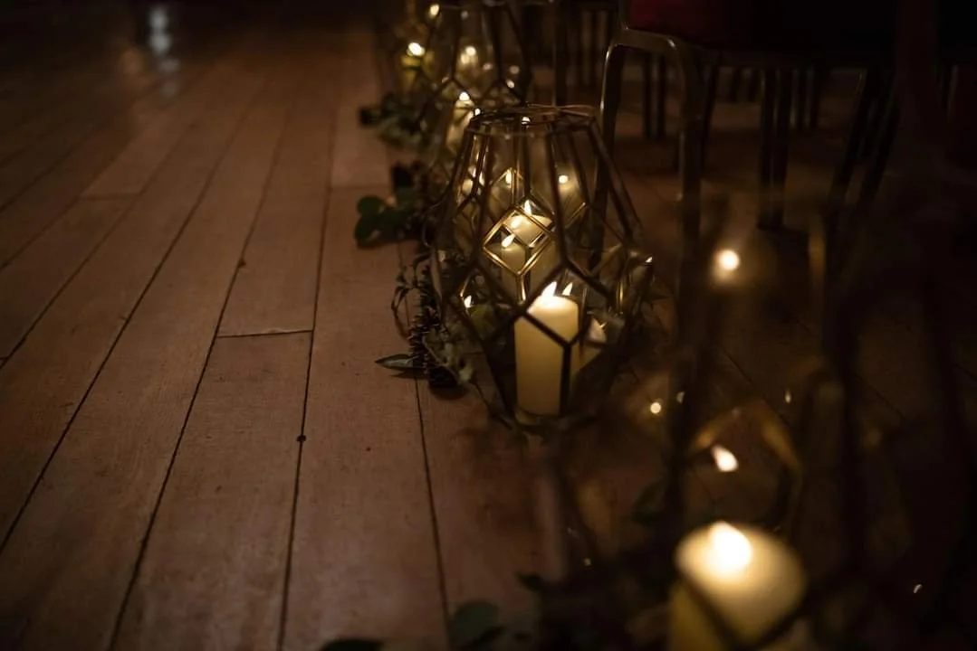 Decorative lanterns with candles inside, along a wooden floor, creating a warm, ambient glow.