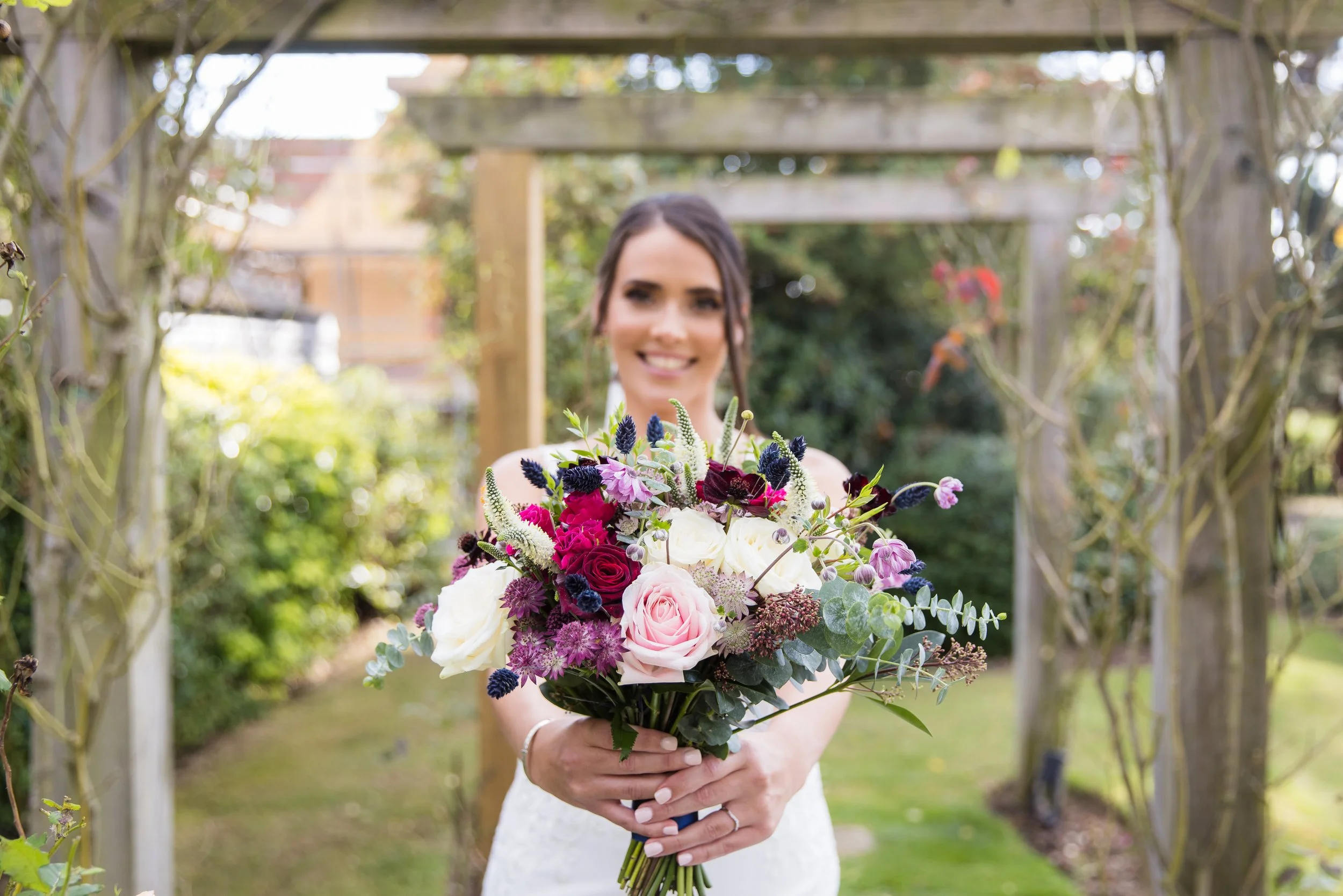 A woman in a wedding dress holding a colorful bouquet of flowers in a garden.