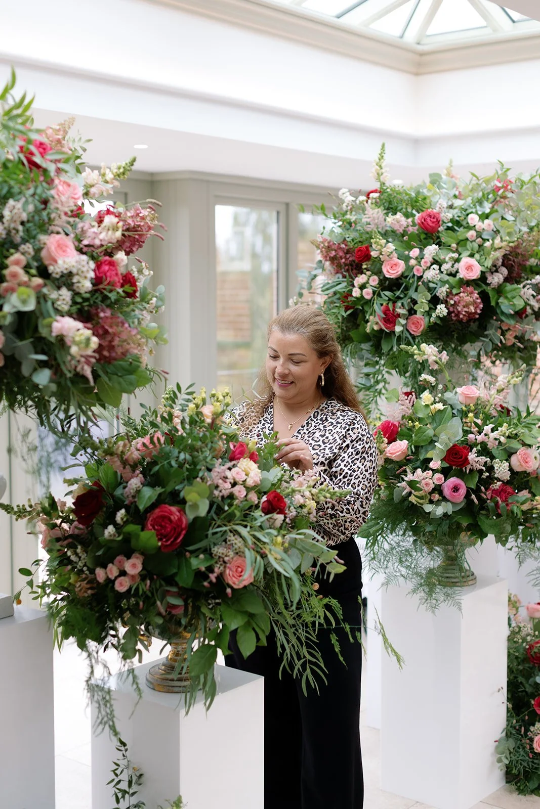 A woman arranging a large bouquet of pink and red flowers inside a bright room.