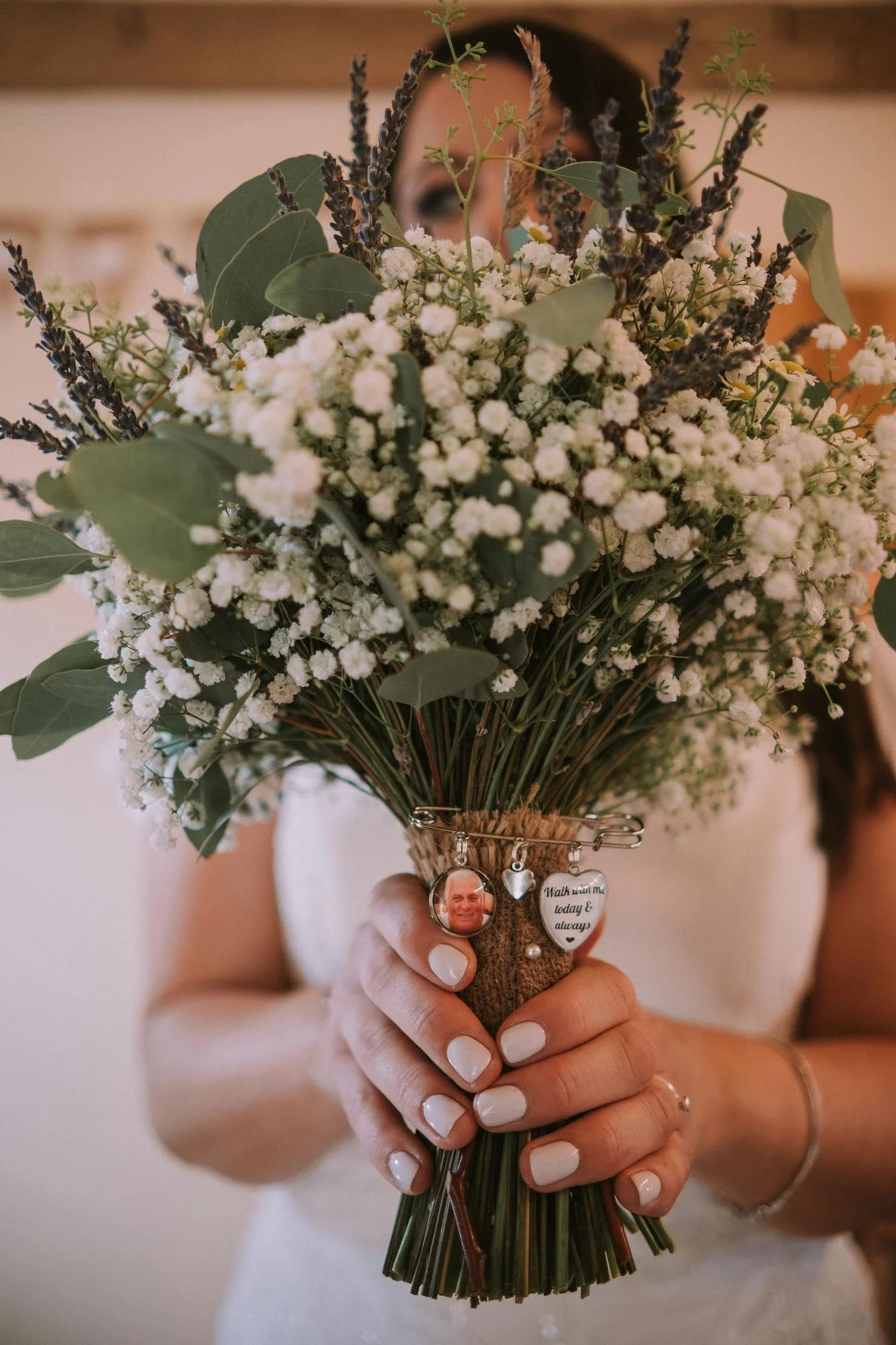 Person holding a bouquet of white flowers and green leaves, with a bracelet and rings on their fingers.