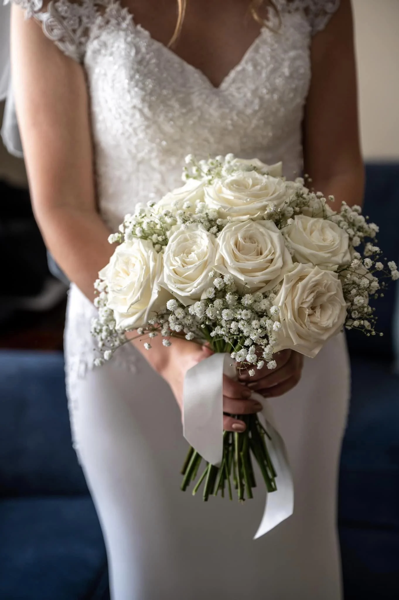 Bride holding a bouquet of white roses and baby's breath in a white wedding dress.