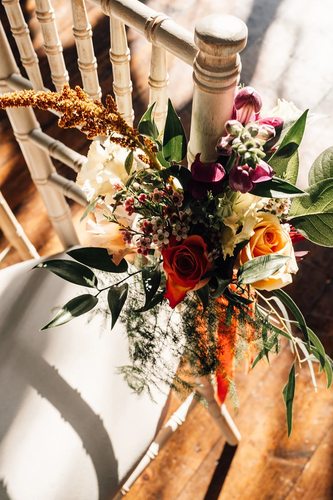 Vase of mixed fresh flowers including roses, snapdragons, and greenery on a white table with a shadow cast nearby.
