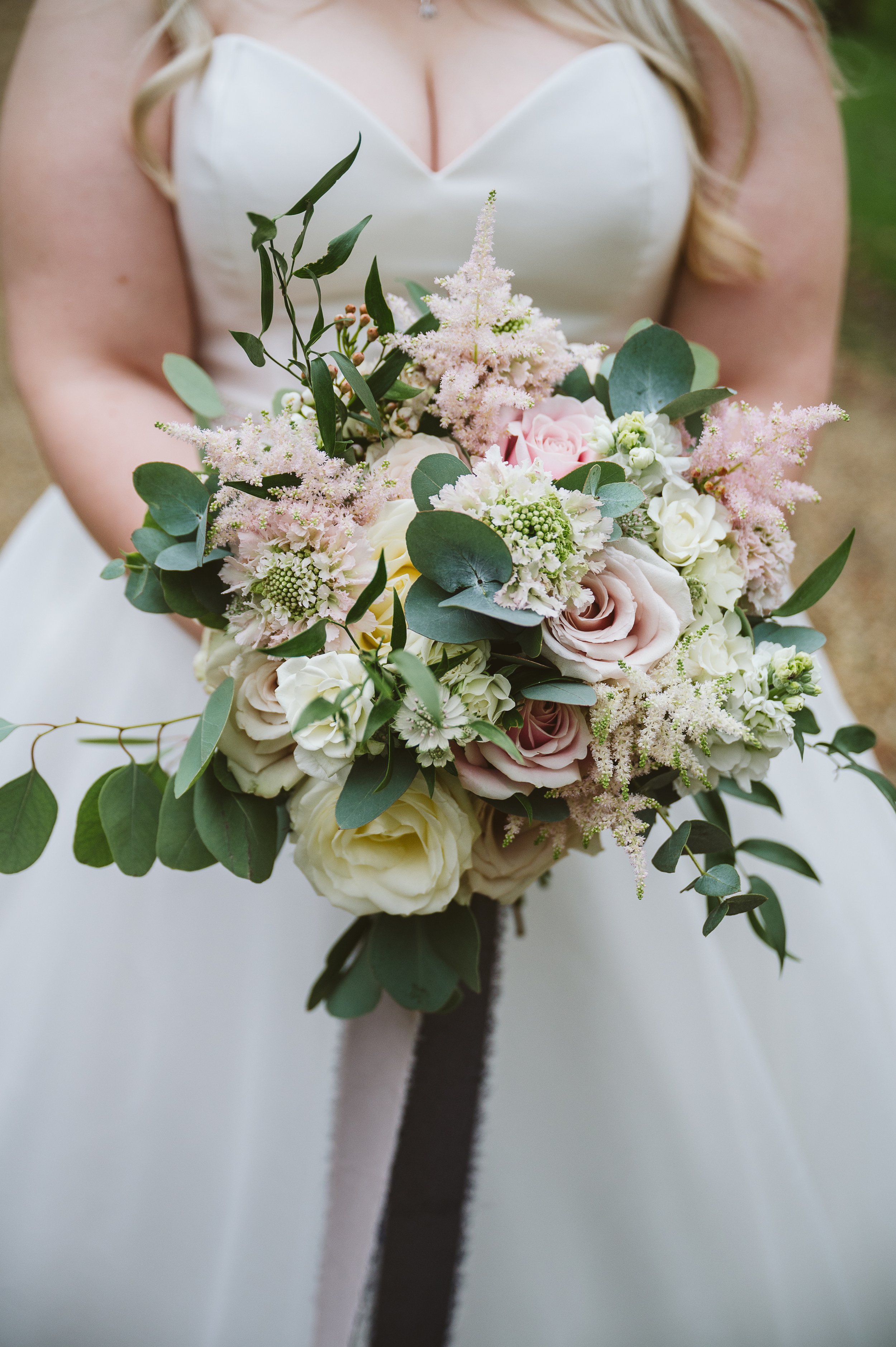 Bride holding a bouquet of pink and white flowers and green foliage.
