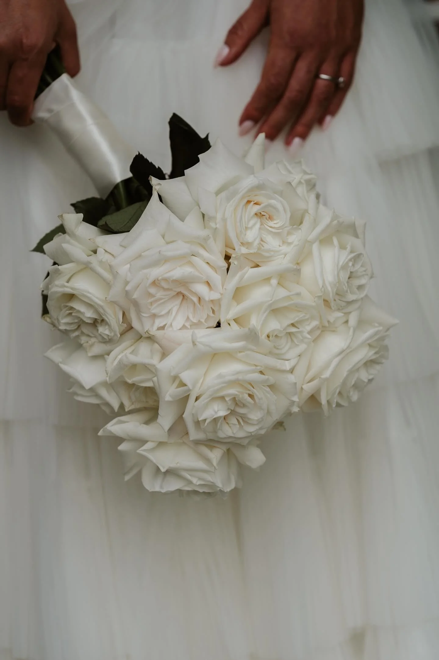 A person holding a bouquet of white roses on a white dress.