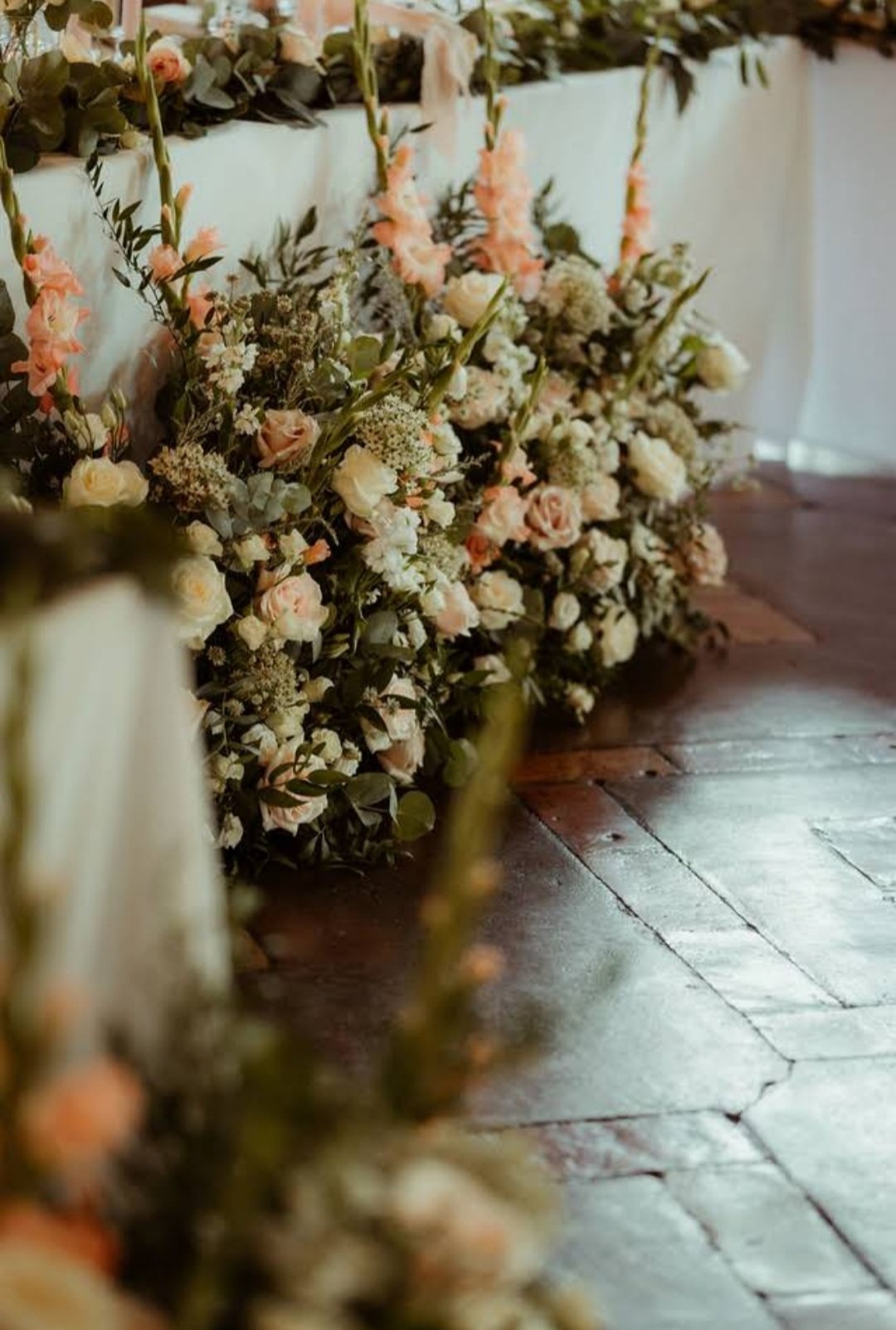 Close-up of a flower arrangement with pink and white flowers along a brick floor.