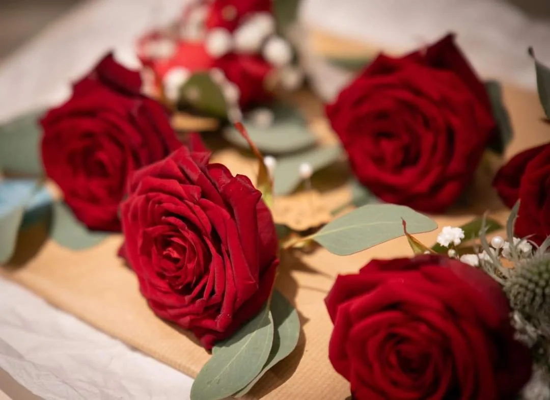 Close-up of red roses and green leaves arranged on a table.