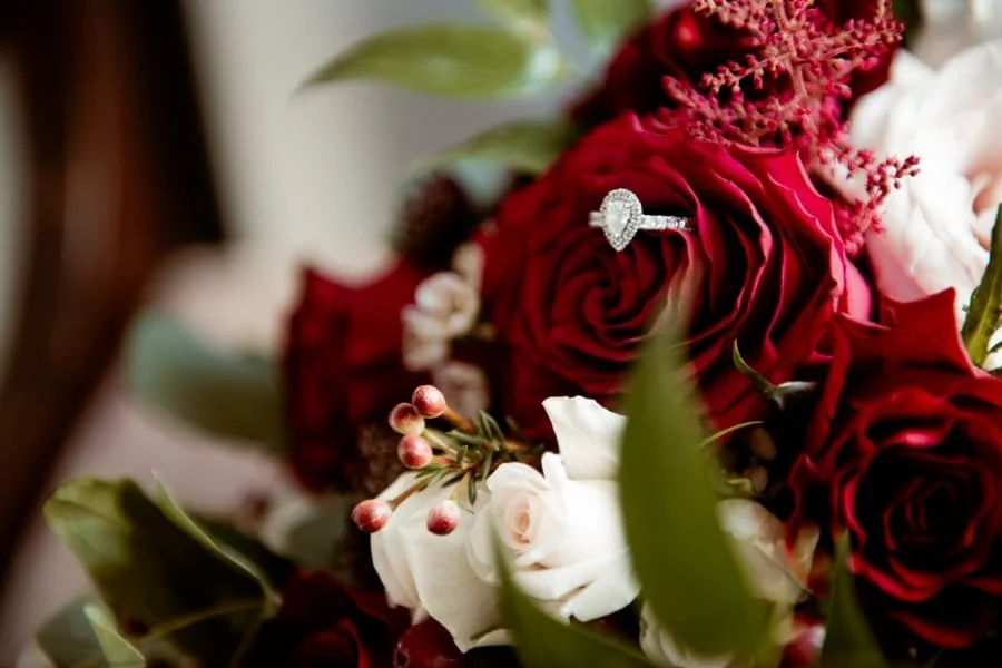 A bouquet of red and white roses with greenery, featuring an engagement ring on a red rose.