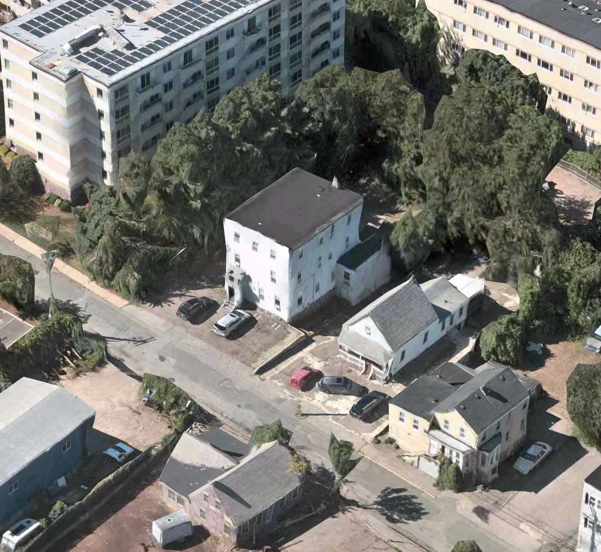 Aerial view of city neighborhood with multi-story buildings, trees, parked cars, and residential houses.