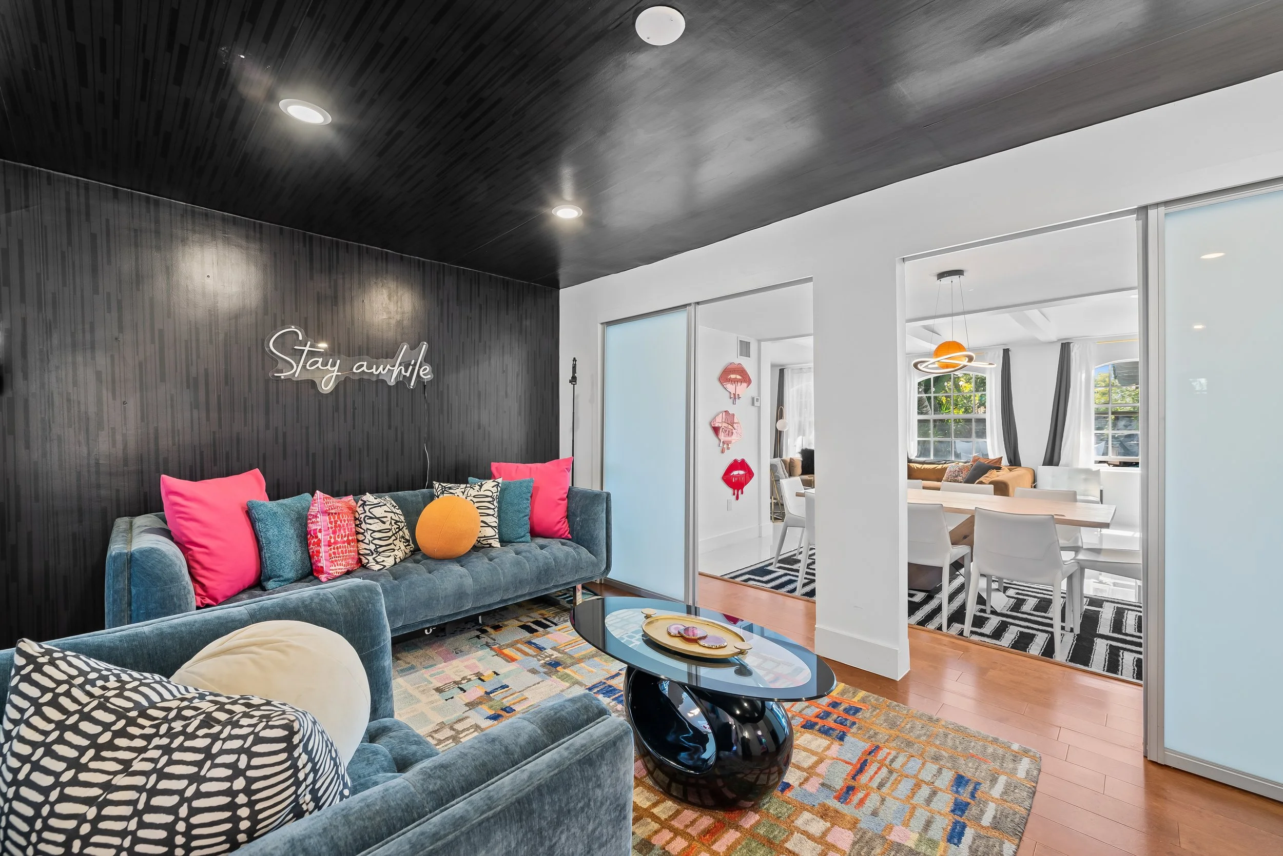Living room with 'Stay Awhile' neon sign and blue velvet sofa — Sun Haven Collection art-inspired vacation rental.