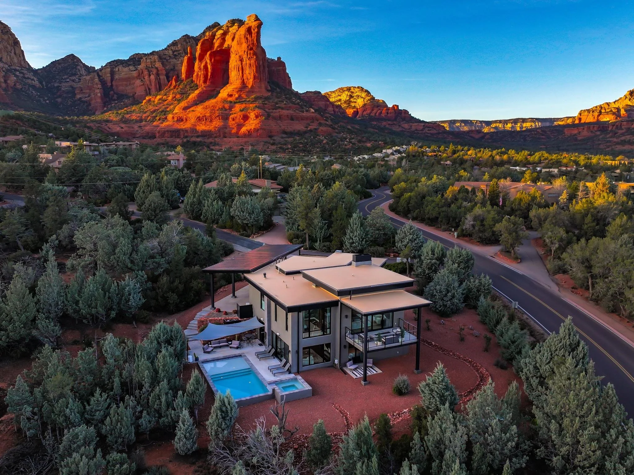 Modern house with a pool in a desert landscape, with red rock formations and mountains in the background.