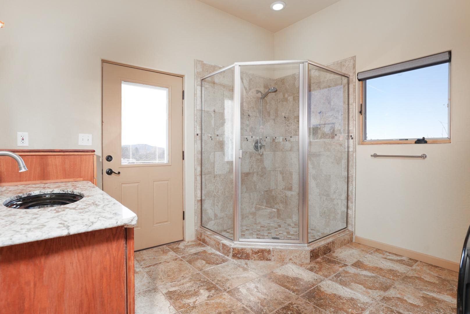 Bathroom with a glass shower enclosure, a window, a door with a window, a towel hanger, and a countertop with a sink.