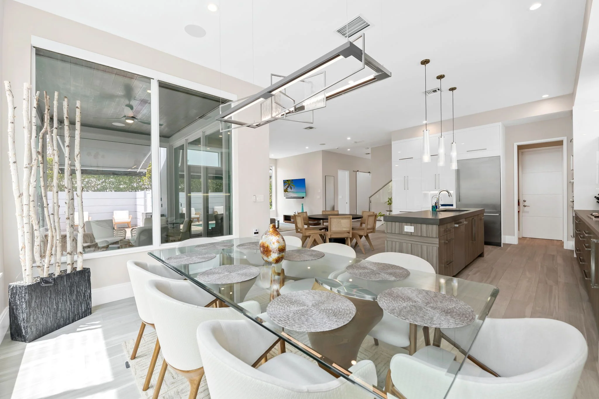 Interior view of a modern open-plan kitchen and dining area with white cabinets, a kitchen island, a round dining table with white chairs, and large glass sliding doors leading to an outdoor patio.