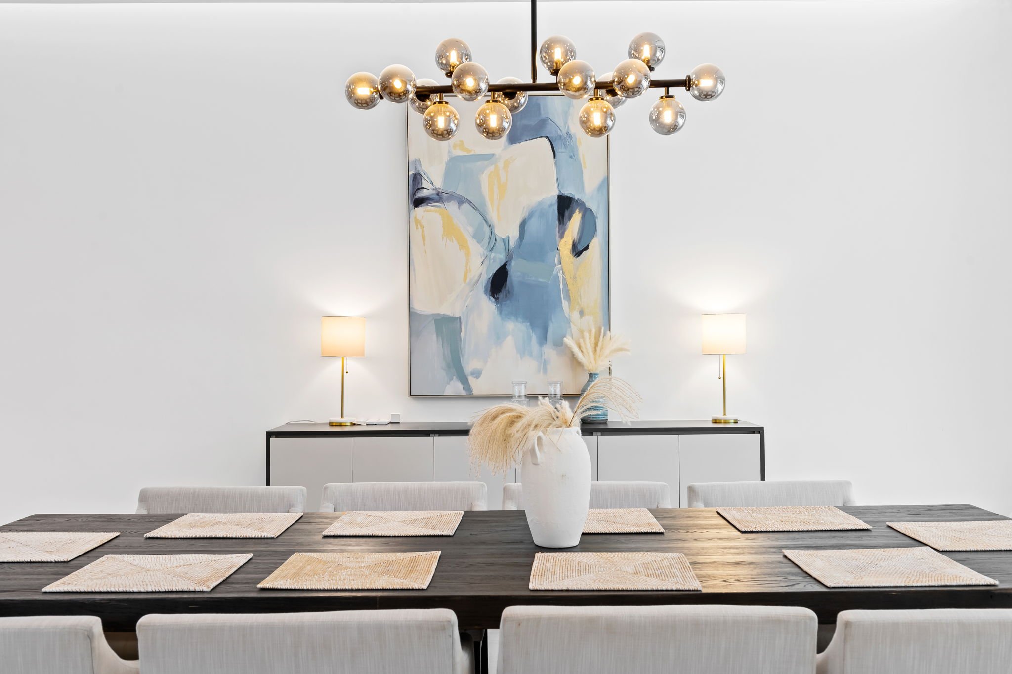 Designer dining room with statement chandelier, abstract art, and pampas grass — luxury vacation rental, Sun Haven Collection.