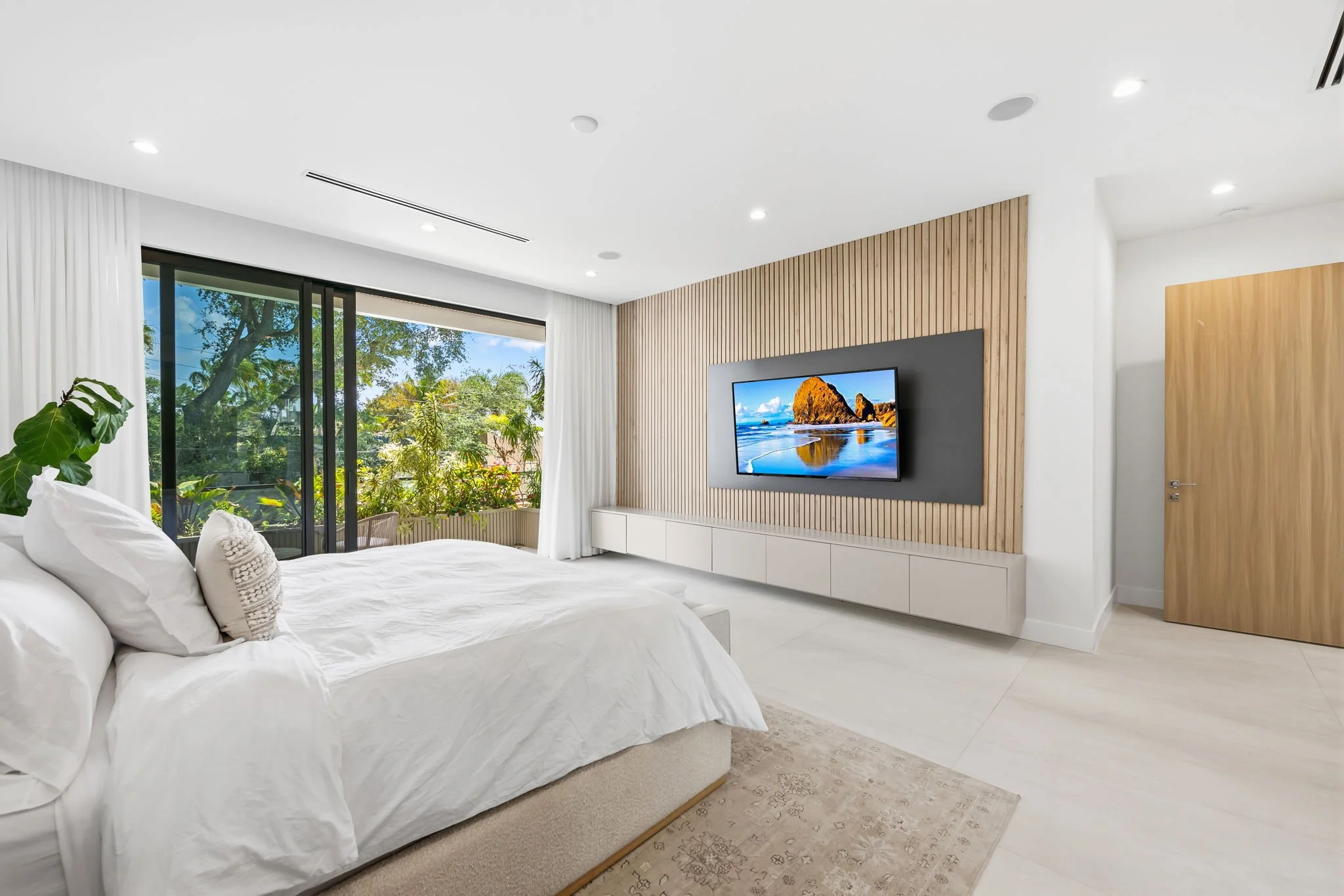 Primary bedroom with wooden accent wall, smart TV, and garden views — Sun Haven Collection luxury vacation home.