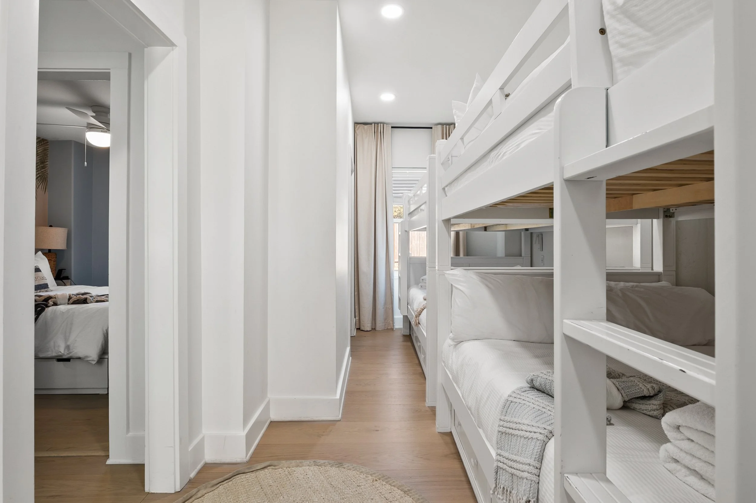 Fitted bunk beds in a bright white bedroom with wooden flooring and beige curtains at the window.