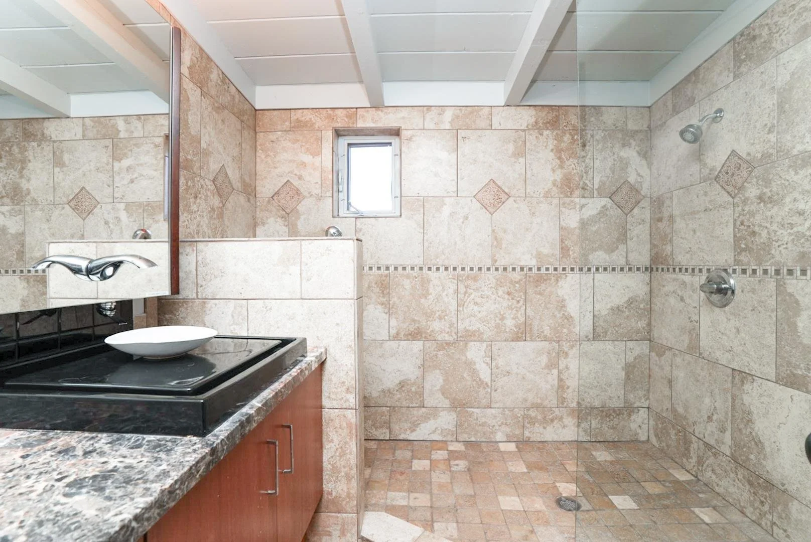 Bathroom with beige stone tiles on walls and floor, a small window, and a glass-enclosed shower area with multiple showerheads.