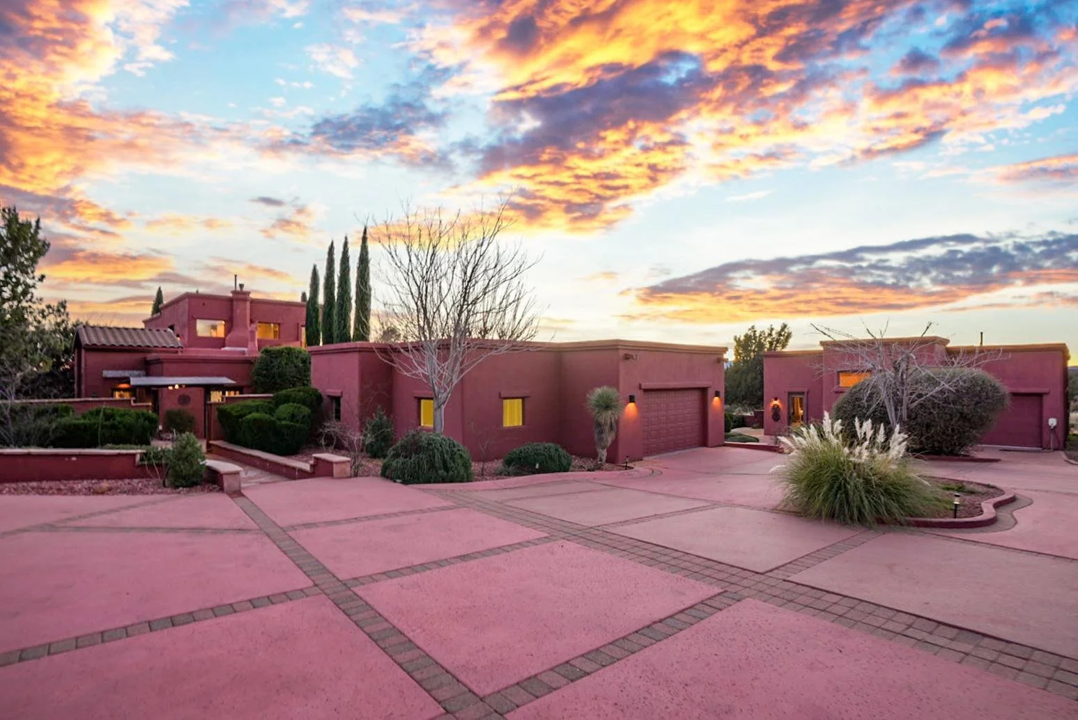 Pink stucco house with desert landscaping, trees, and cacti, under a colorful sunset sky.