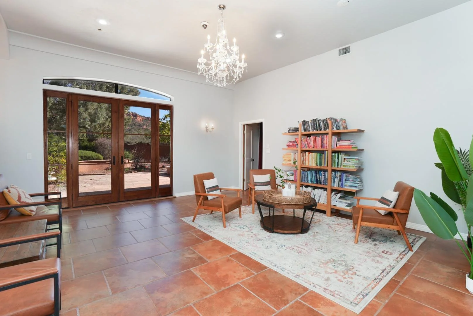 Living room with large wooden sliding glass doors, a chandelier, a bookshelf, and a seating area with armchairs and a rug.