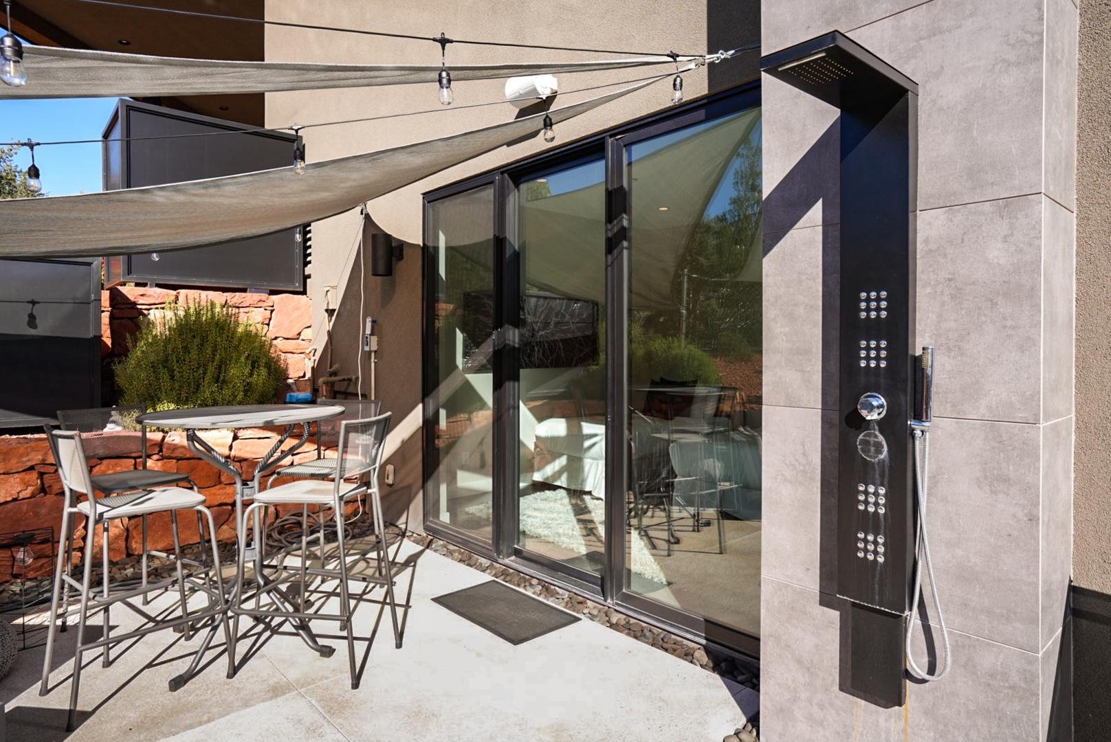 Outdoor patio with metal table and chairs, sliding glass door, and outdoor shower with black panel and handheld showerhead.
