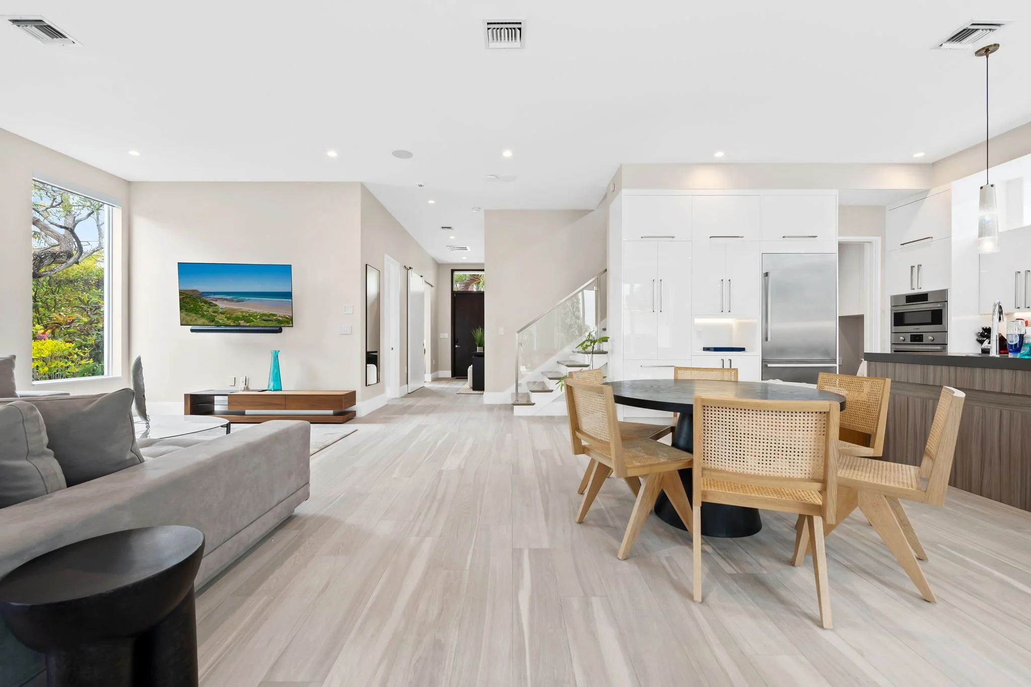 Open-plan living, dining, and kitchen with beach-themed TV — luxury vacation home, Sun Haven Collection.