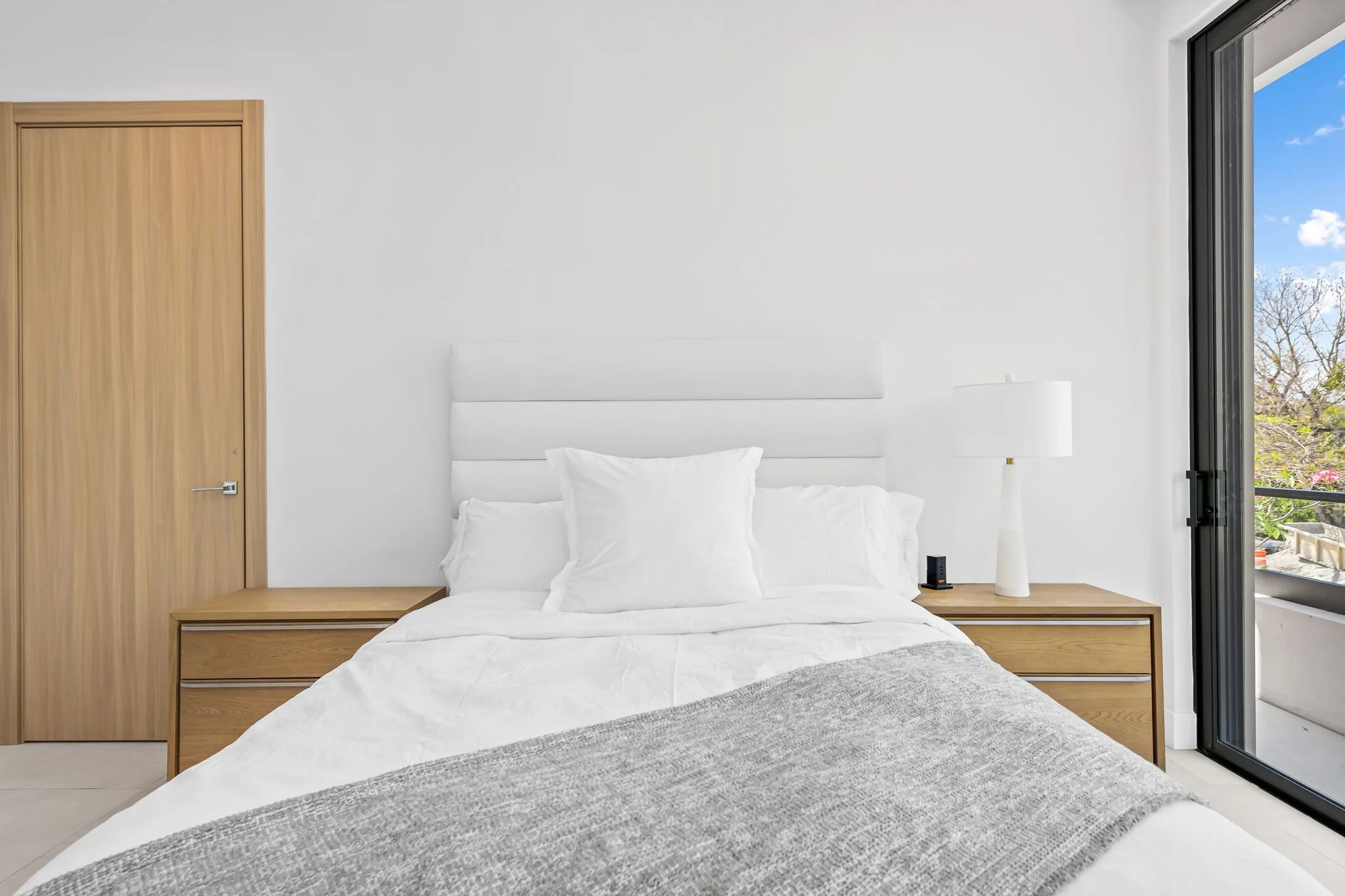 Bedroom with private balcony, wooden headboard, and treetop views — design-forward vacation home, Sun Haven Collection.