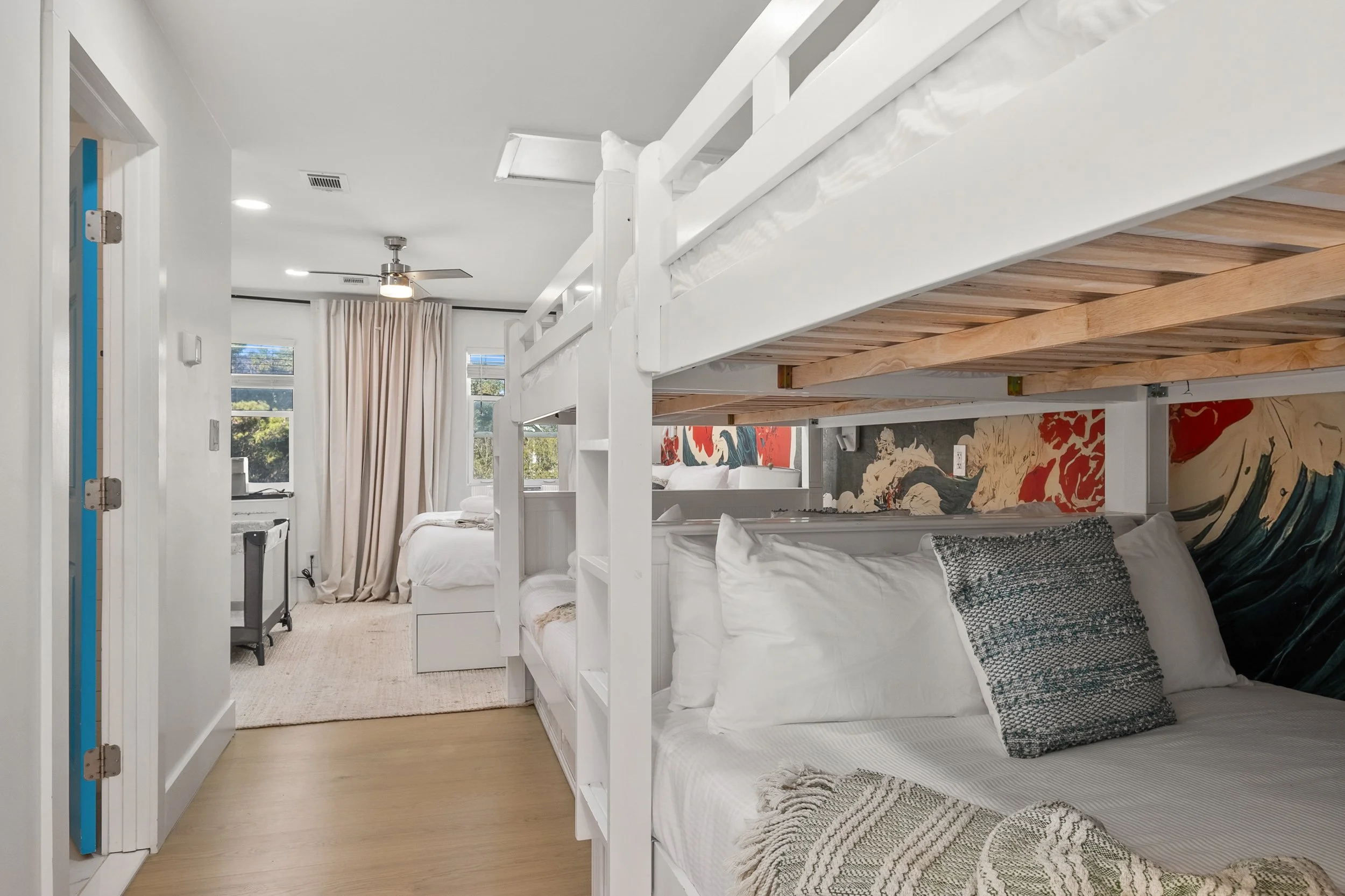 Bedroom with bunk beds, a bed with white sheets, a window with beige curtains, and a ceiling fan.