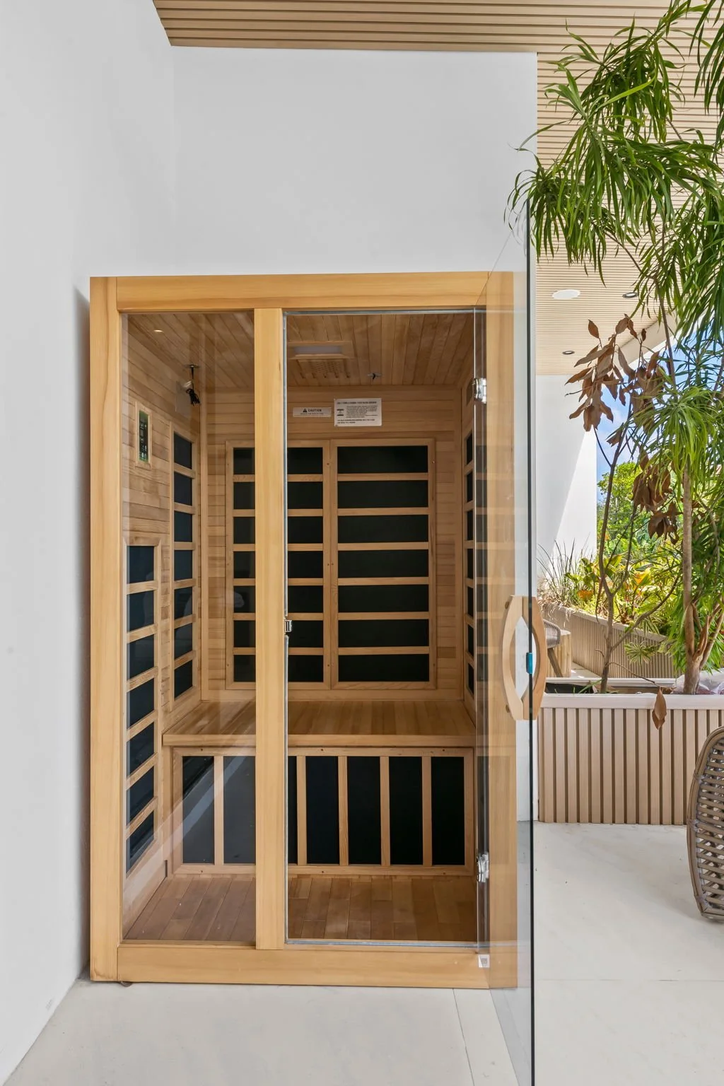 Wooden infrared sauna with glass door inside a modern room with plants