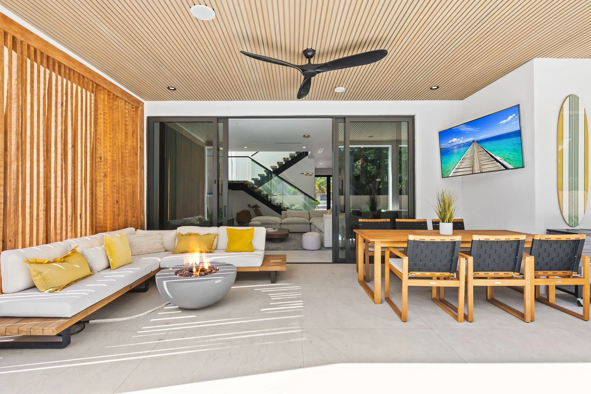 Indoor-outdoor living area with fire pit table, ceiling fan, and coastal decor — Sun Haven Collection luxury vacation rental.