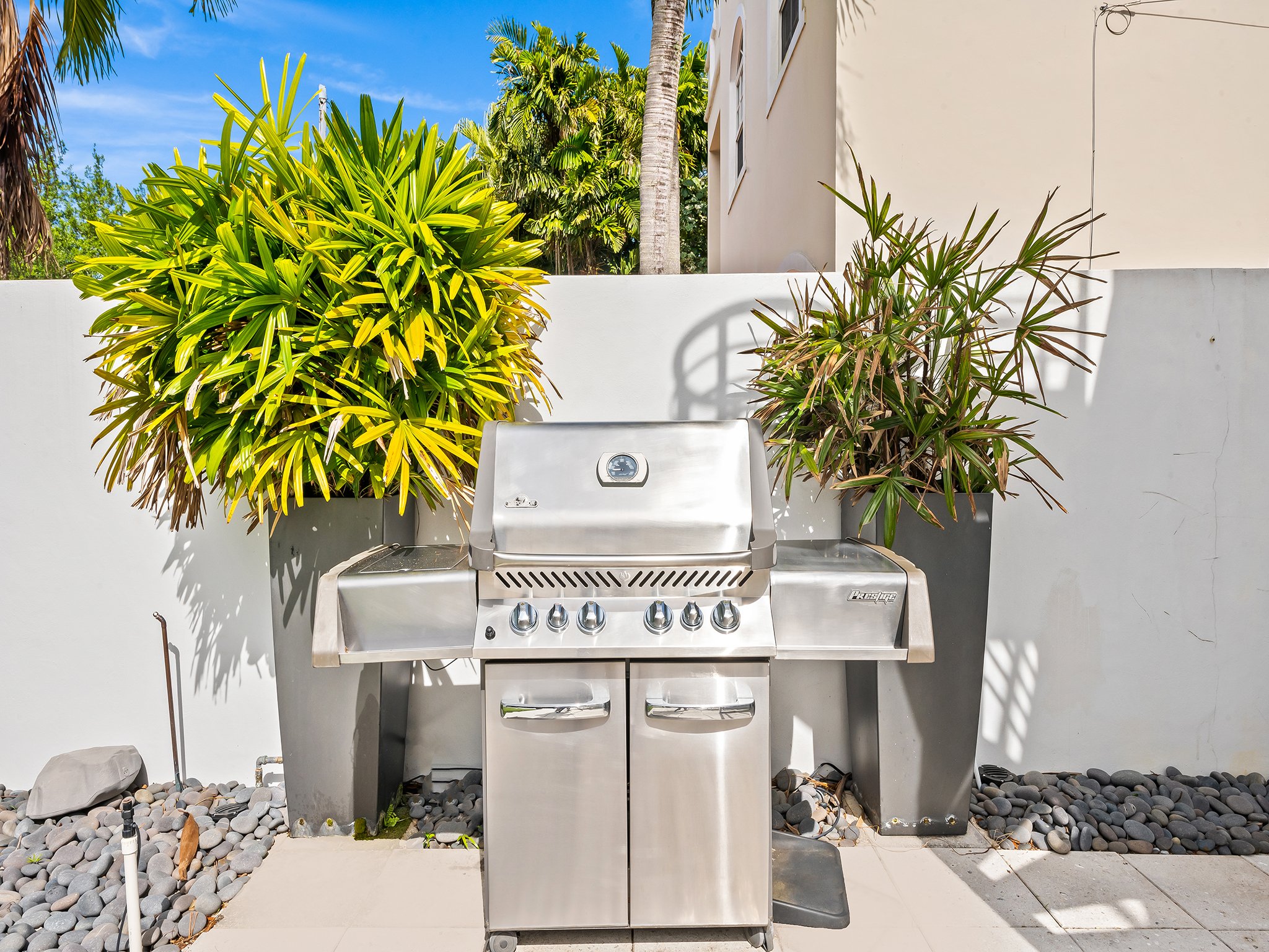 Outdoor stainless steel BBQ grill with tropical landscaping — Sun Haven Collection luxury vacation rental.