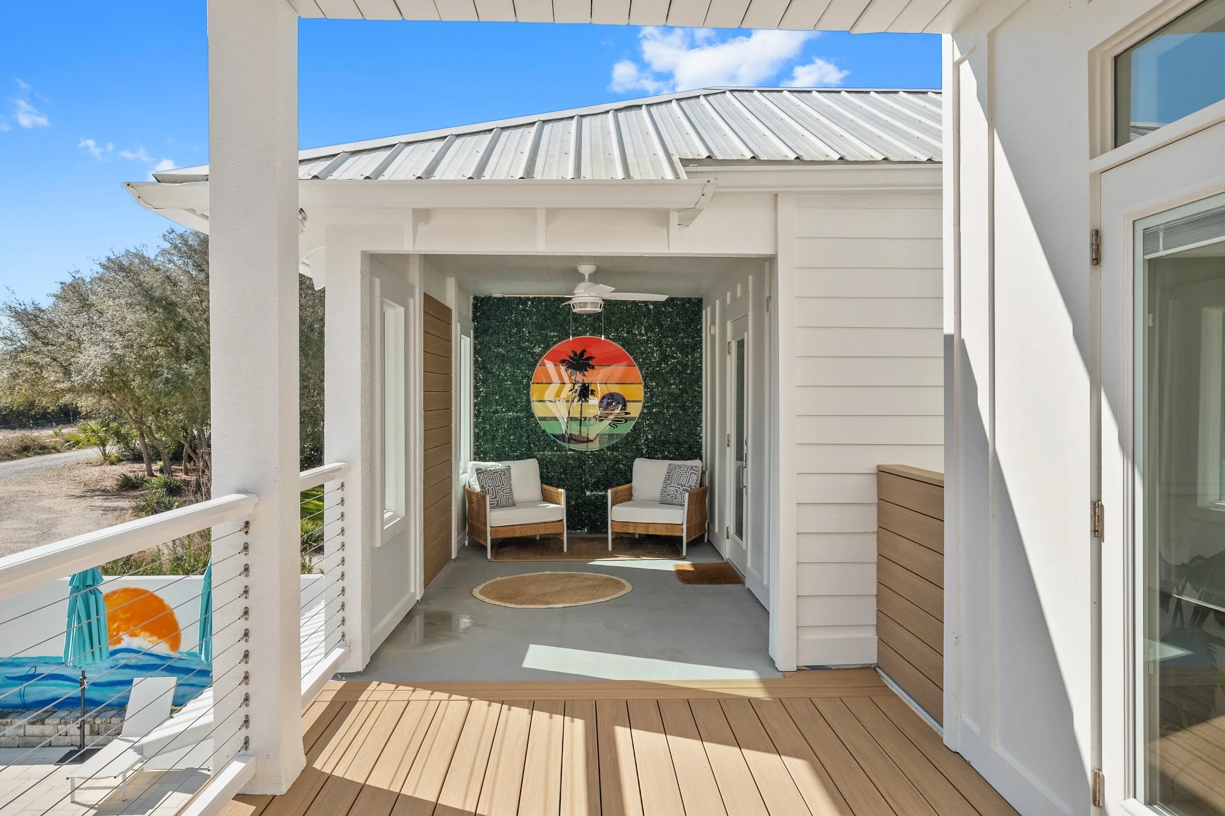 Covered porch area with two armchairs and decorative wall art of a sunset, palm trees, and ocean scene.