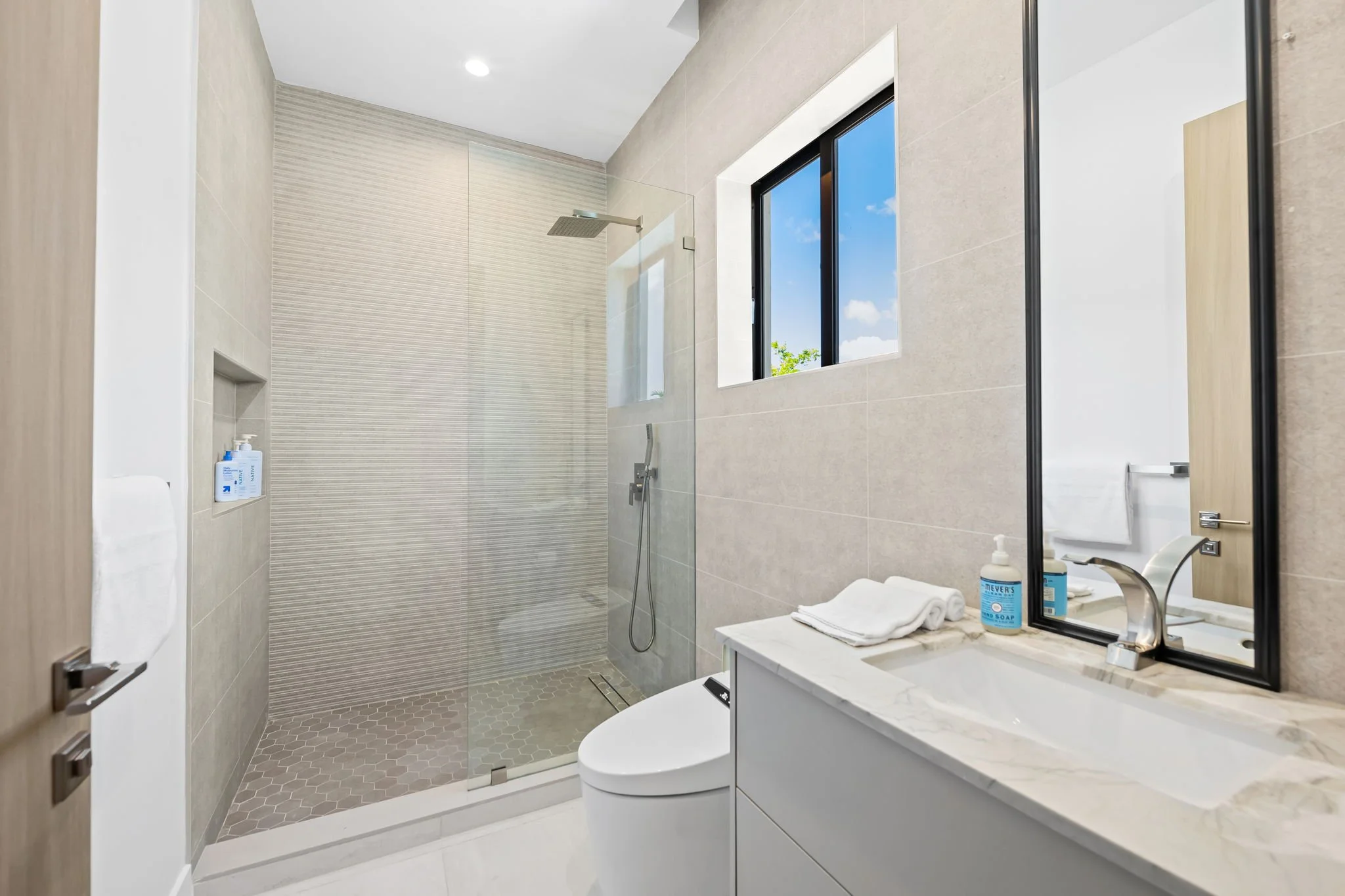 Spa bathroom with rainfall shower, marble vanity, and natural light — Sun Haven Collection luxury vacation rental.