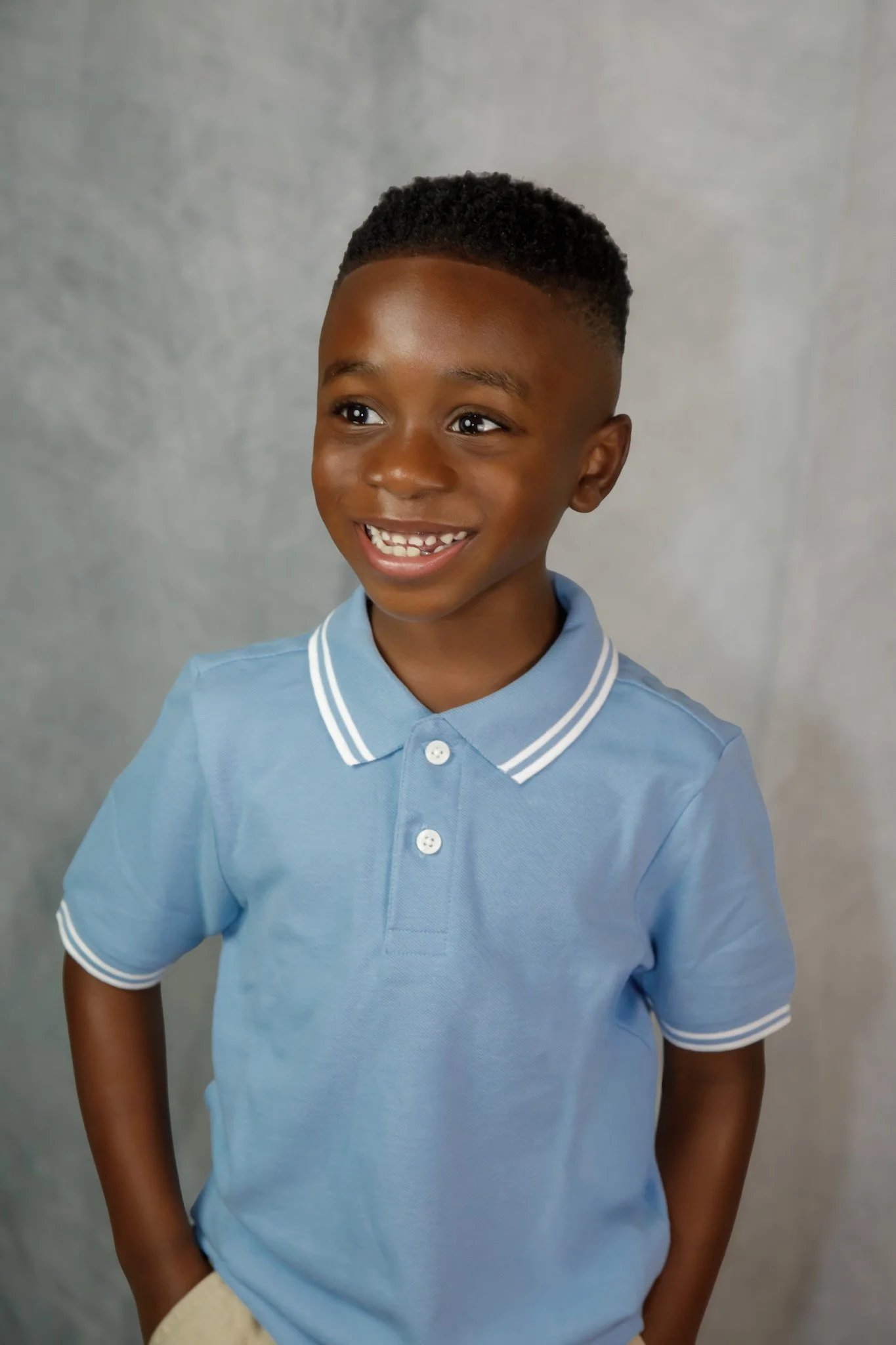 a young kid, posing and smiling, wearing a blue shirt, and khaki pants, with short hair