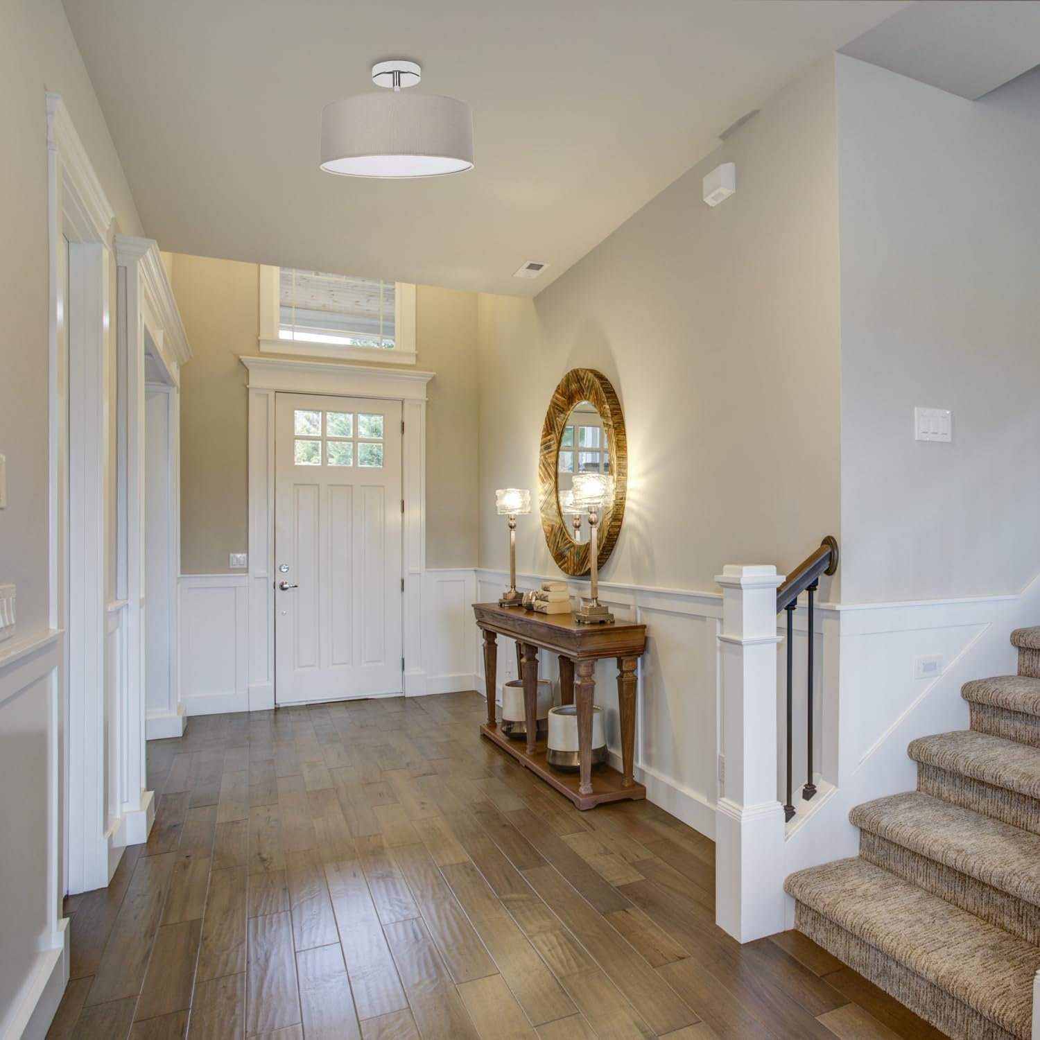 Entryway with a wooden console table, a large round mirror, two table lamps, and a staircase with carpeted steps.
