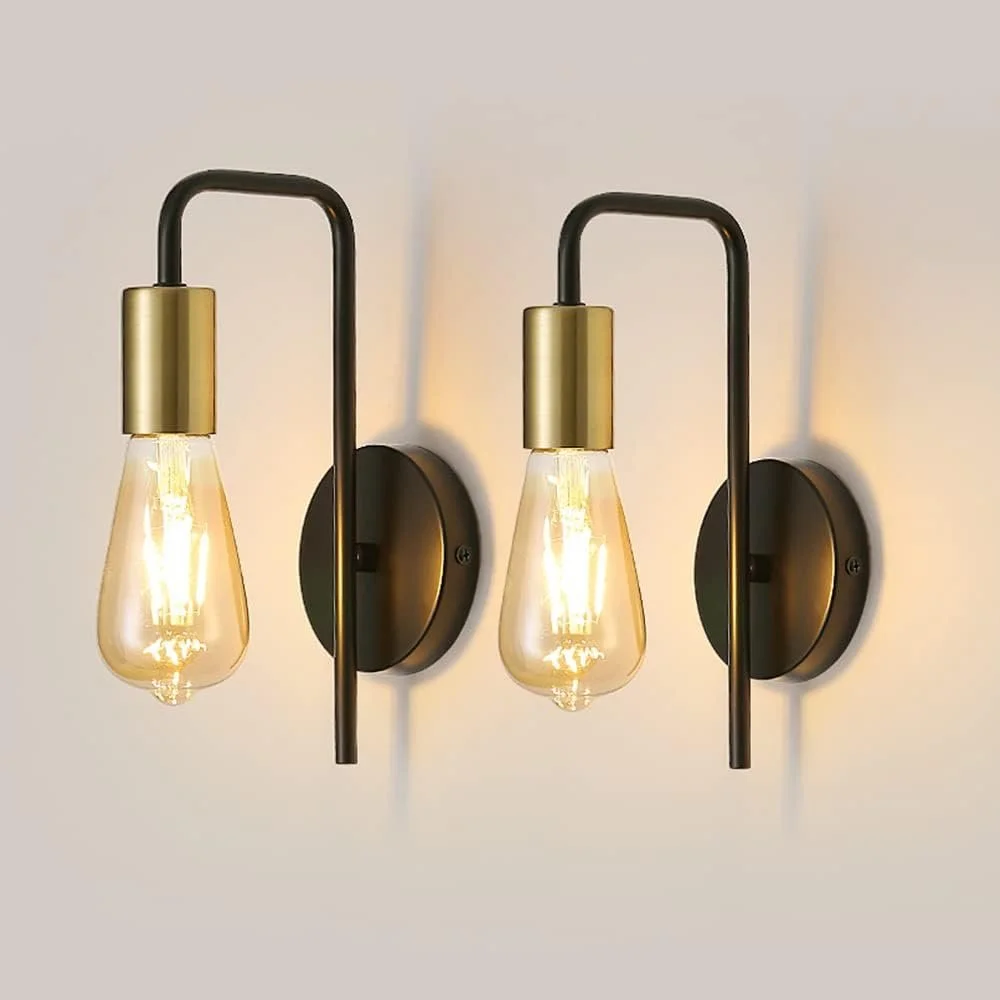 Two modern wall sconces with exposed bulbs and black and gold accents mounted on a white wall.