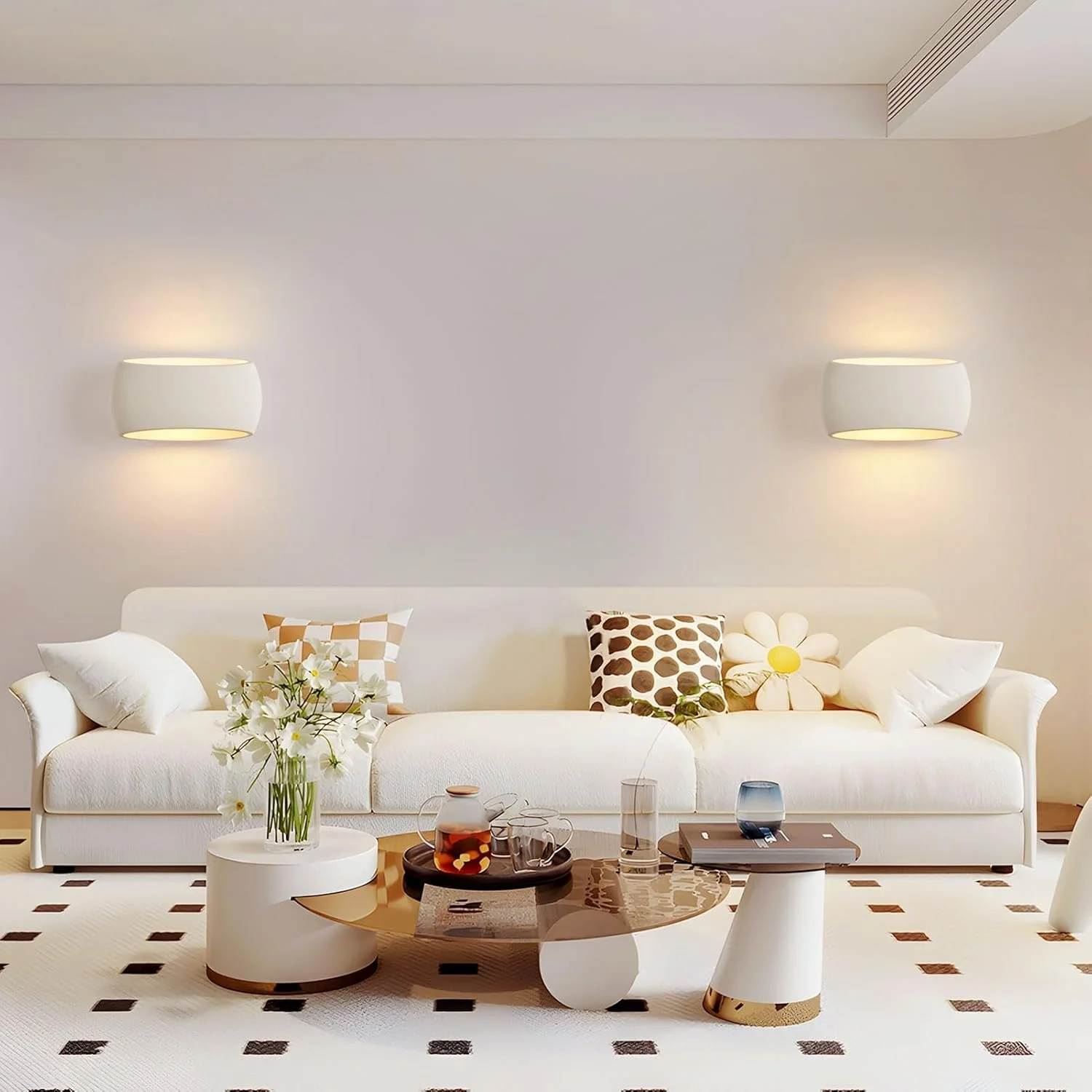 Modern living room with a white sofa decorated with patterned pillows, a coffee table with decorative items, and wall-mounted lights.