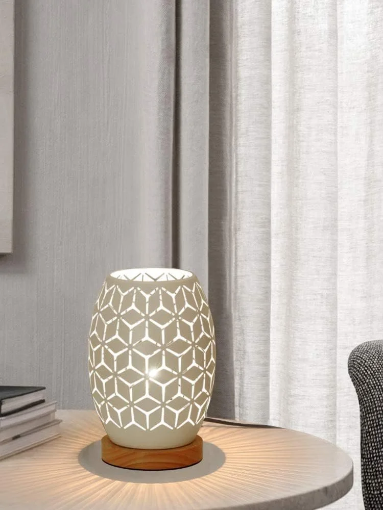 A decorative table lamp with a geometric pattern, placed on a round wooden base on a light-colored table, in front of curtains.