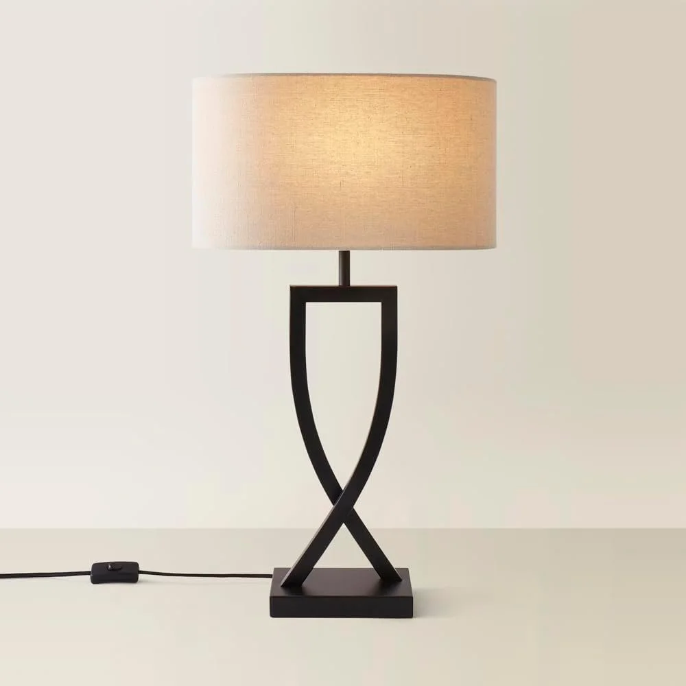 Table lamp with a beige shade and black sculptural base on a white surface.