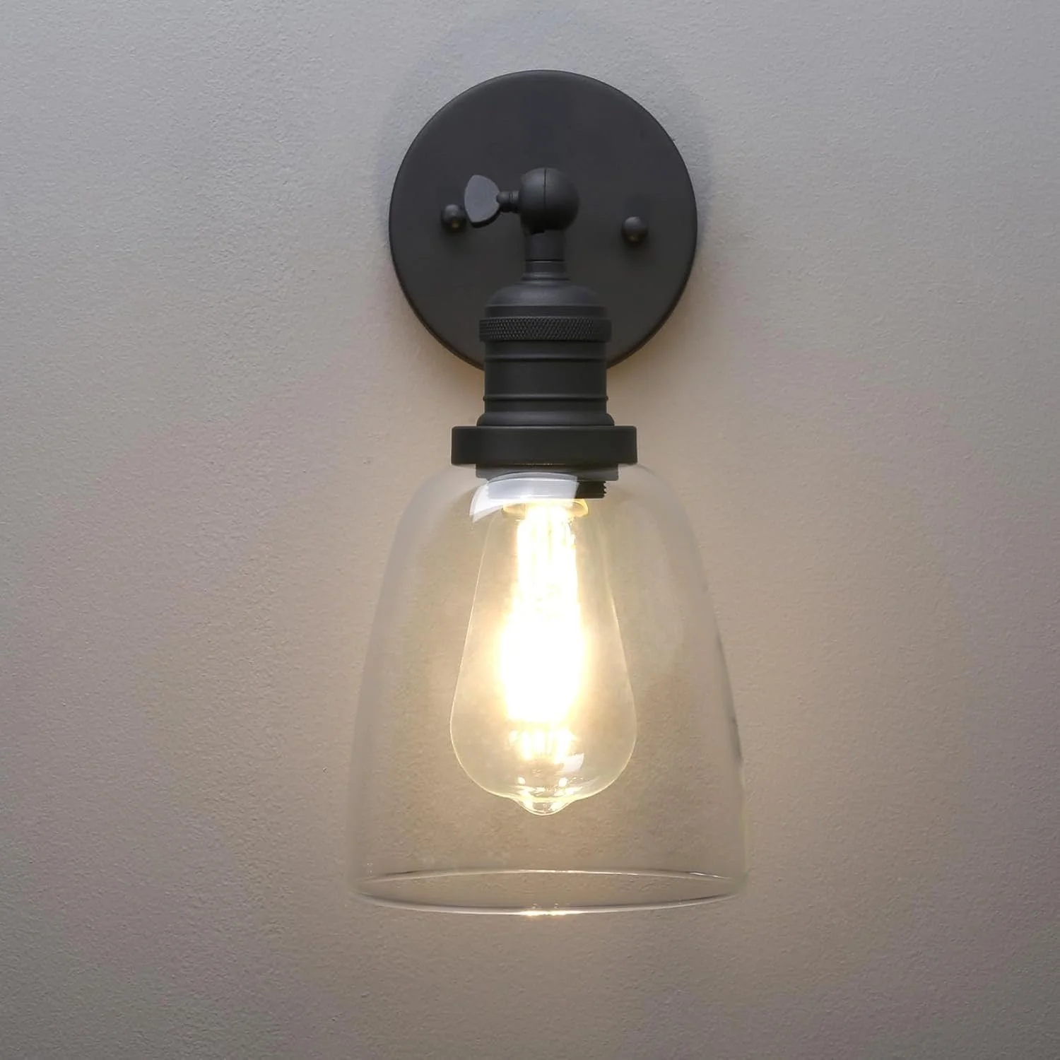 A wall-mounted light fixture with an exposed light bulb and a clear glass shade.