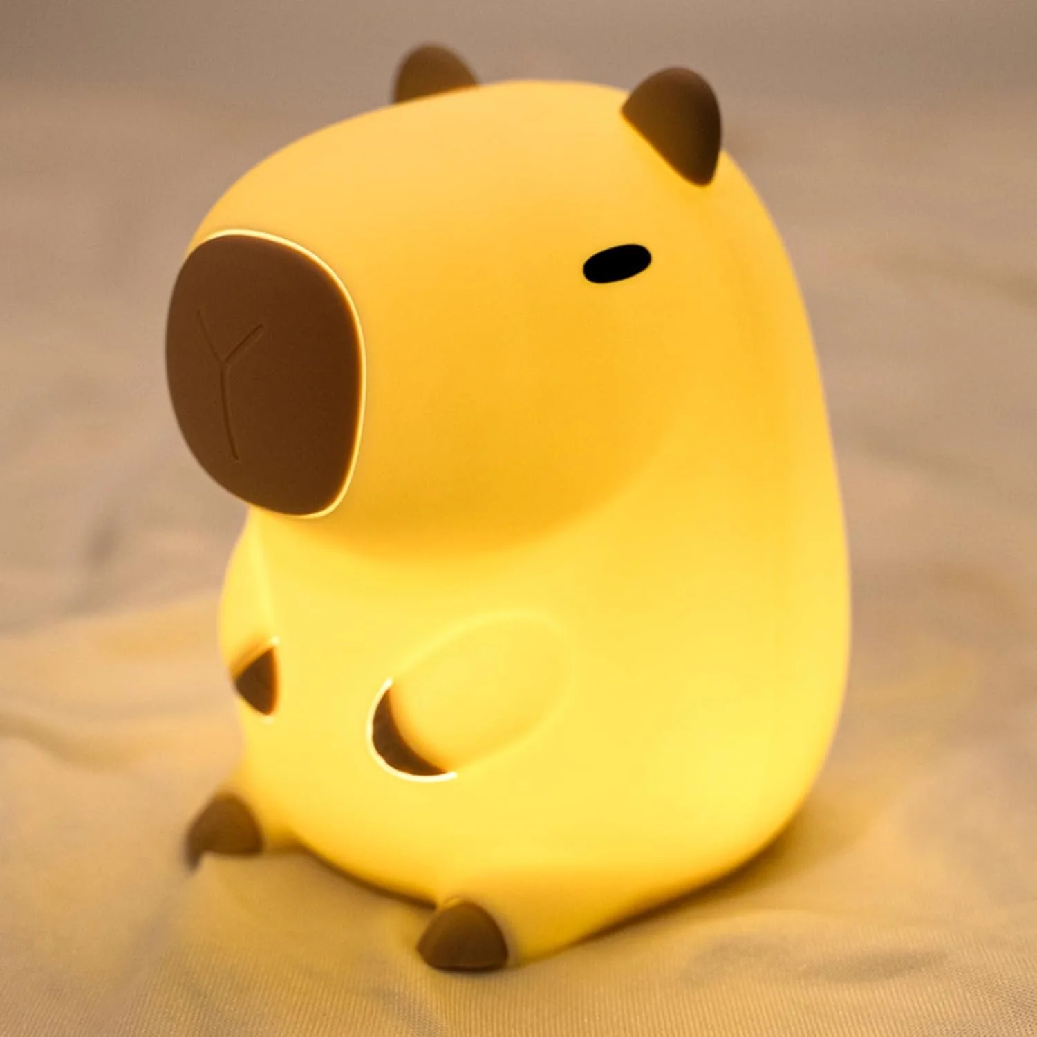 A small, yellow, bear-shaped nightlight with black ears, nose, paw pads, and tail sitting on a surface.
