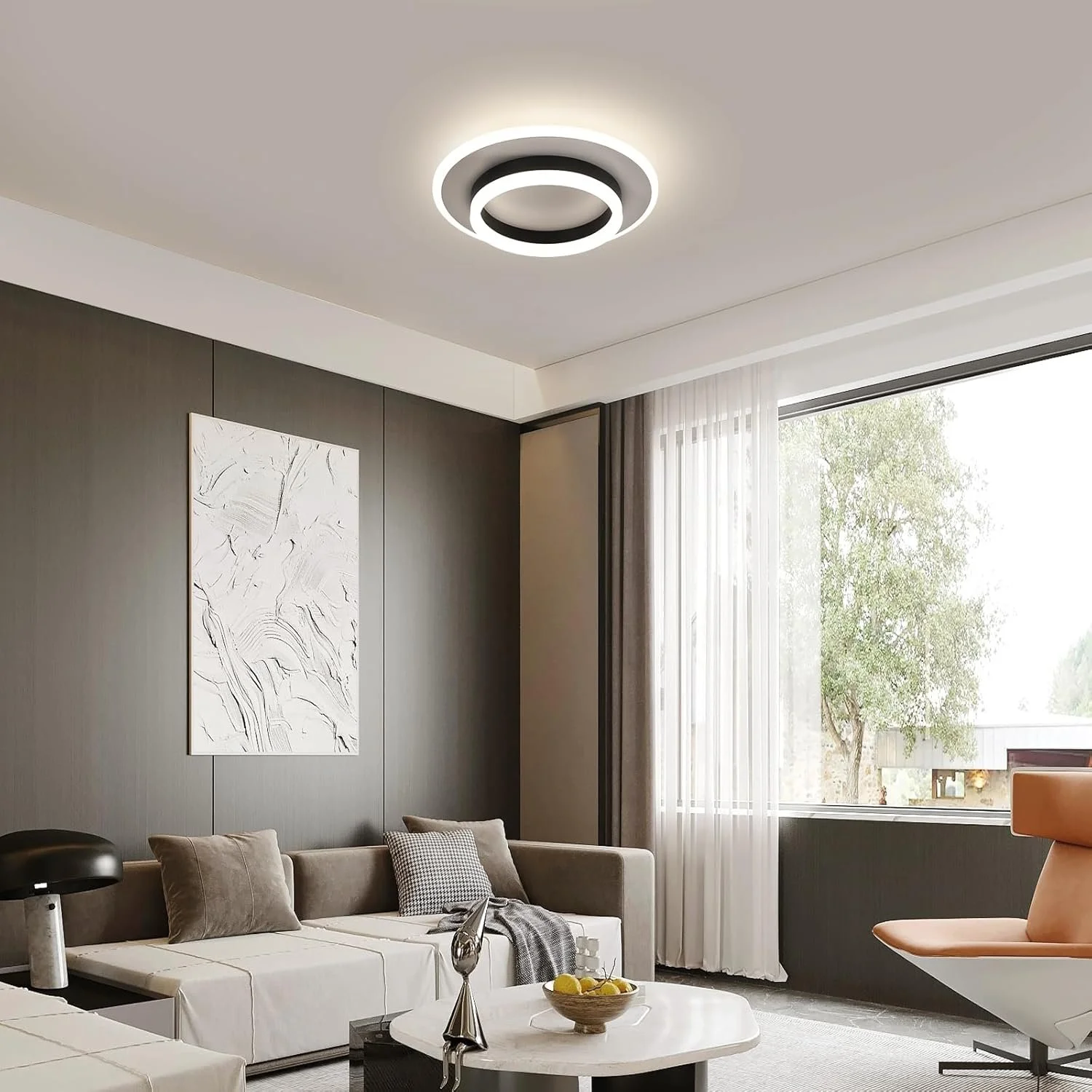 Modern living room with beige sofa, decorative pillows, white curtains, and a round coffee table with lemon and a silver sculpture, illuminated by a circular ceiling light.