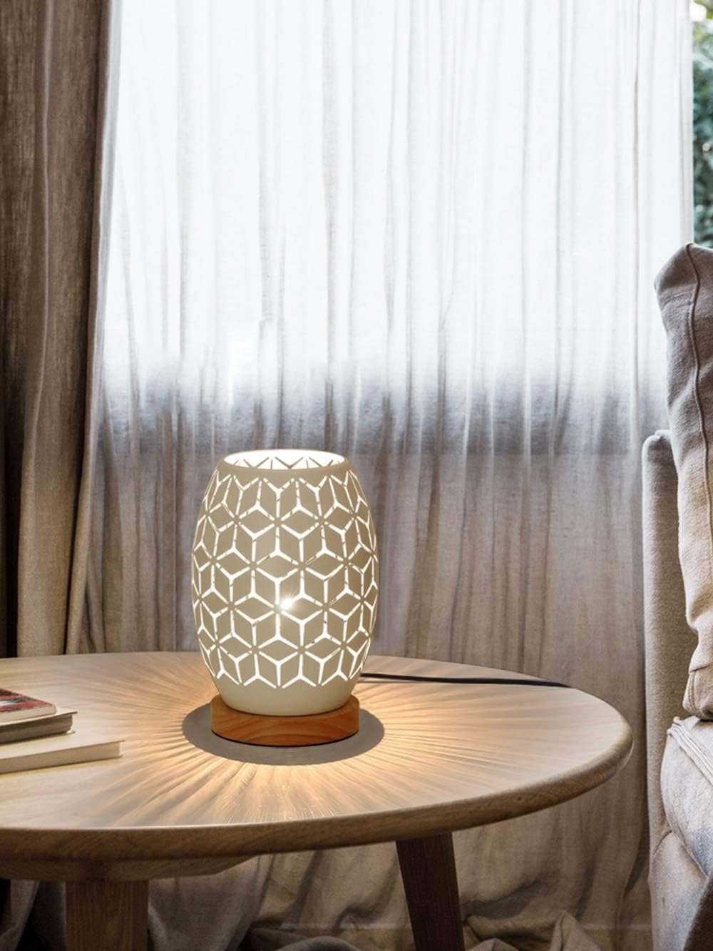 Decorative table lamp with geometric cut-out design on a wooden round table, next to a cream-colored couch, with sheer curtains in the background letting diffuse natural light into the room.