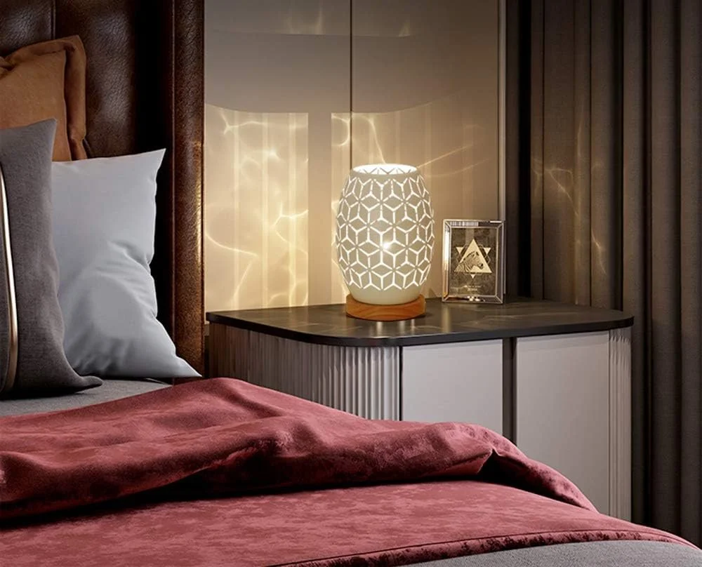 A bedroom with a bed covered in red velvet bedding, a white pillow, a brown headboard, and a nightstand with a decorative white lamp and a framed photograph.