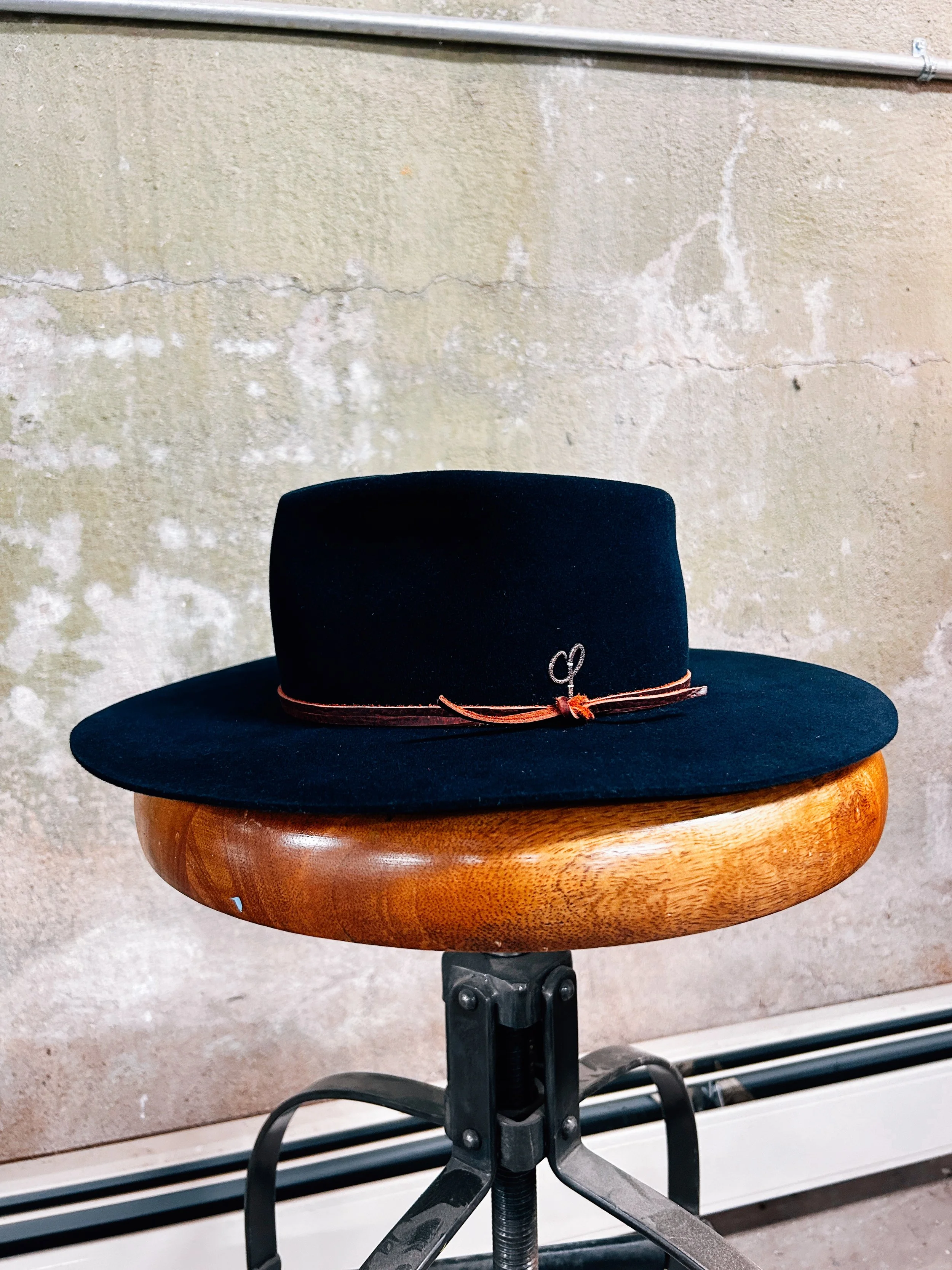 Black wide-brimmed hat with a thin brown band resting on a round wooden stool.